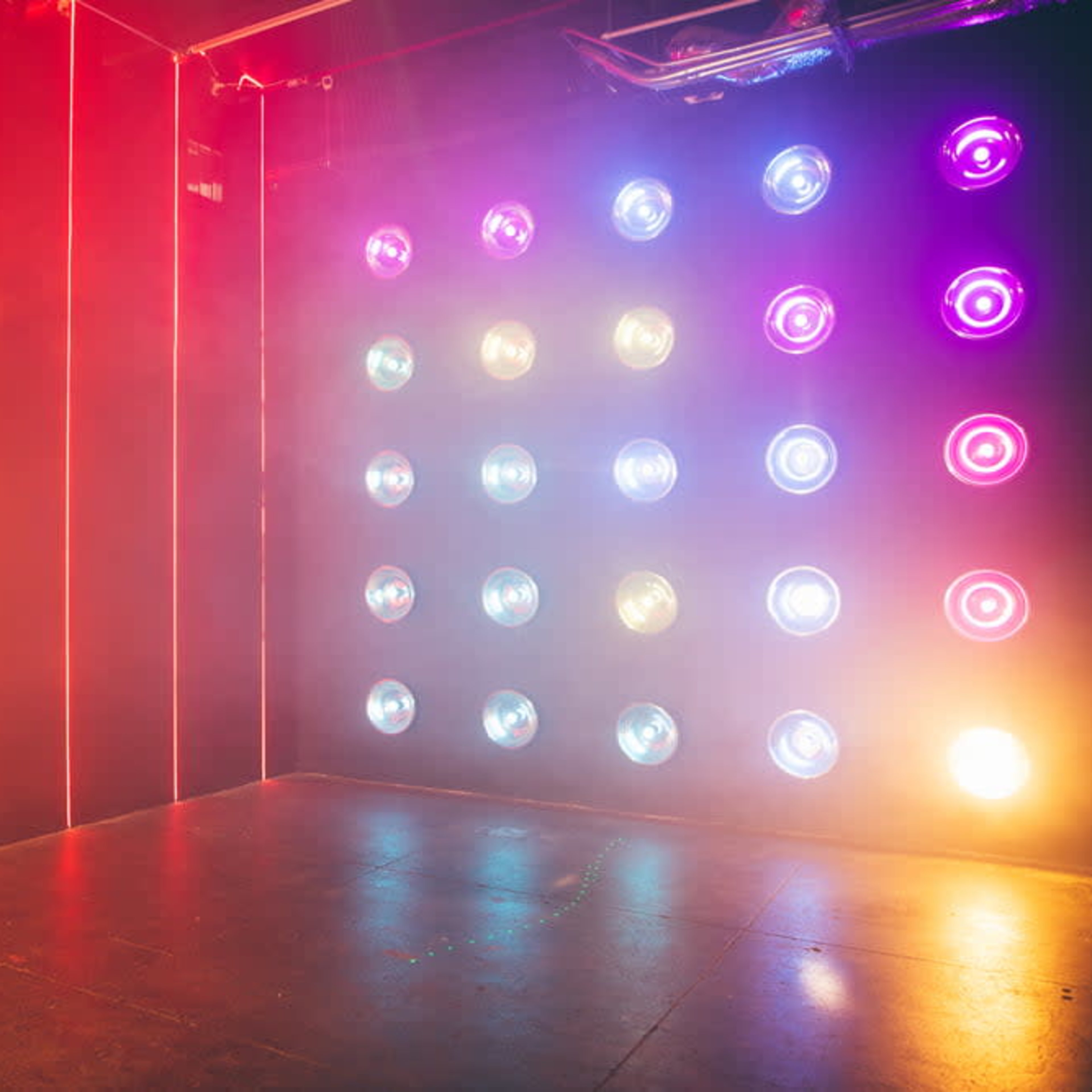 A room features three walls illuminated with colorful lights and a grid of circular light fixtures on the fourth wall.