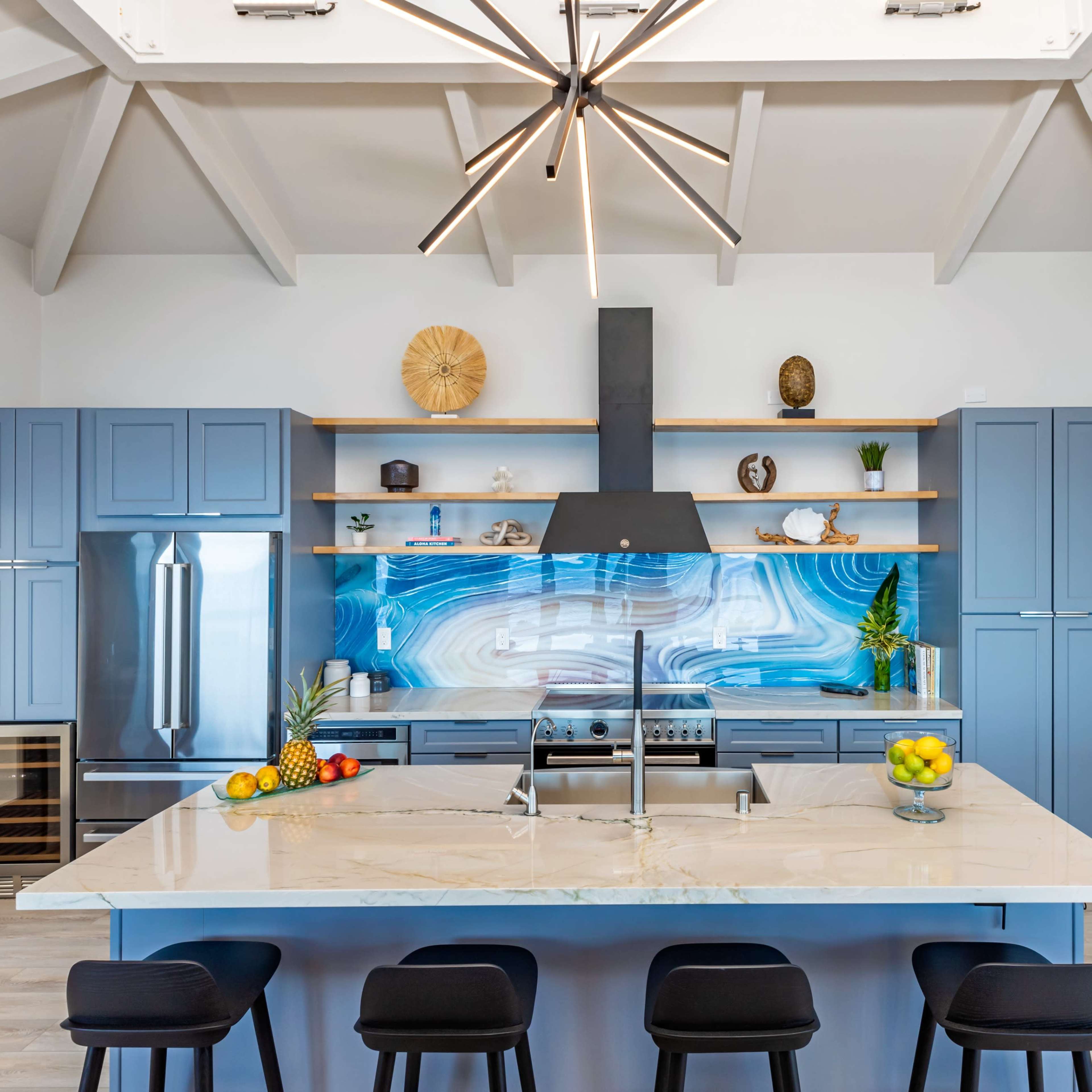 The kitchen features a large island with a marble countertop, blue cabinetry, an intricate backsplash, and modern pendant lighting.