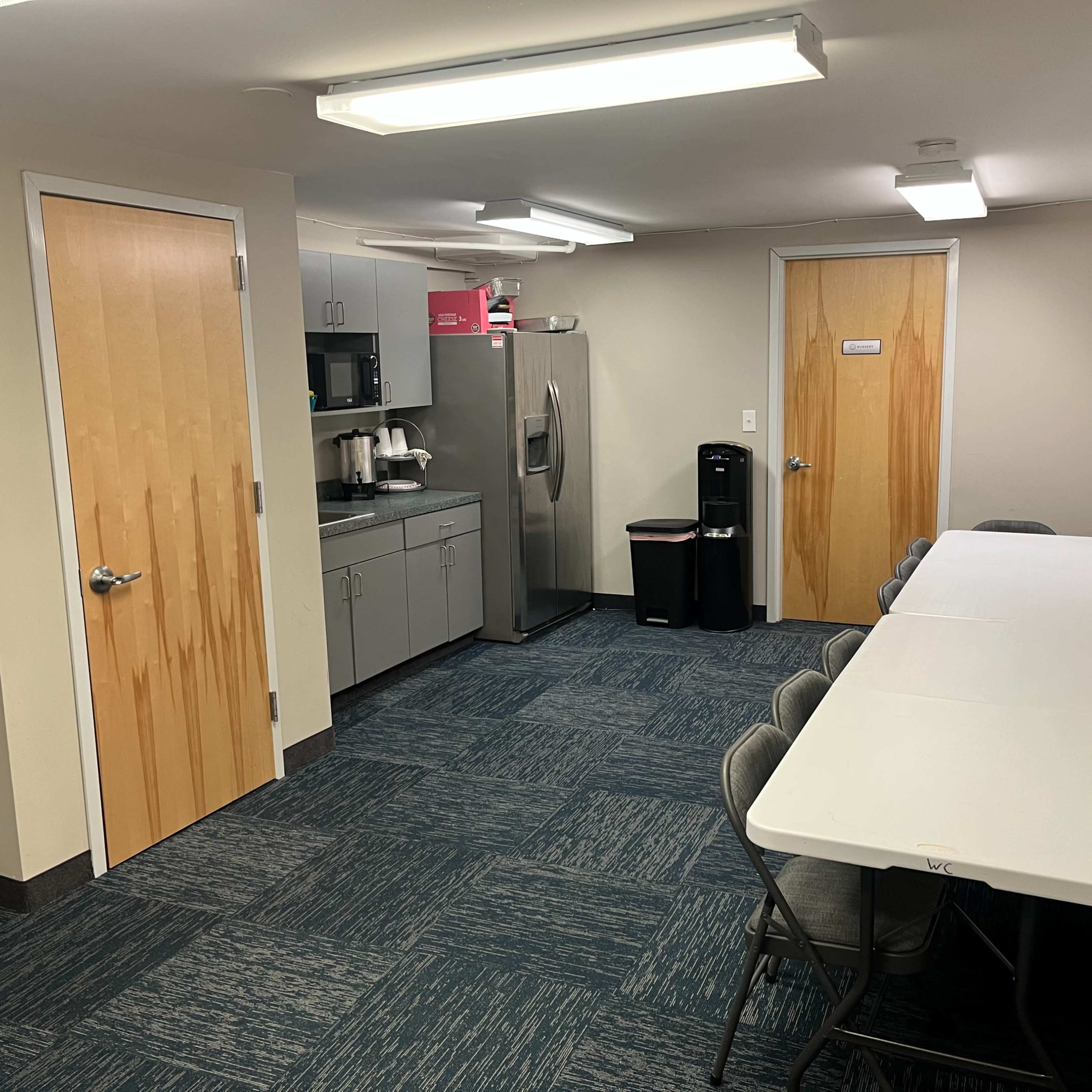 A break room features a long table with chairs, a kitchenette with appliances, and two doors leading to other areas.