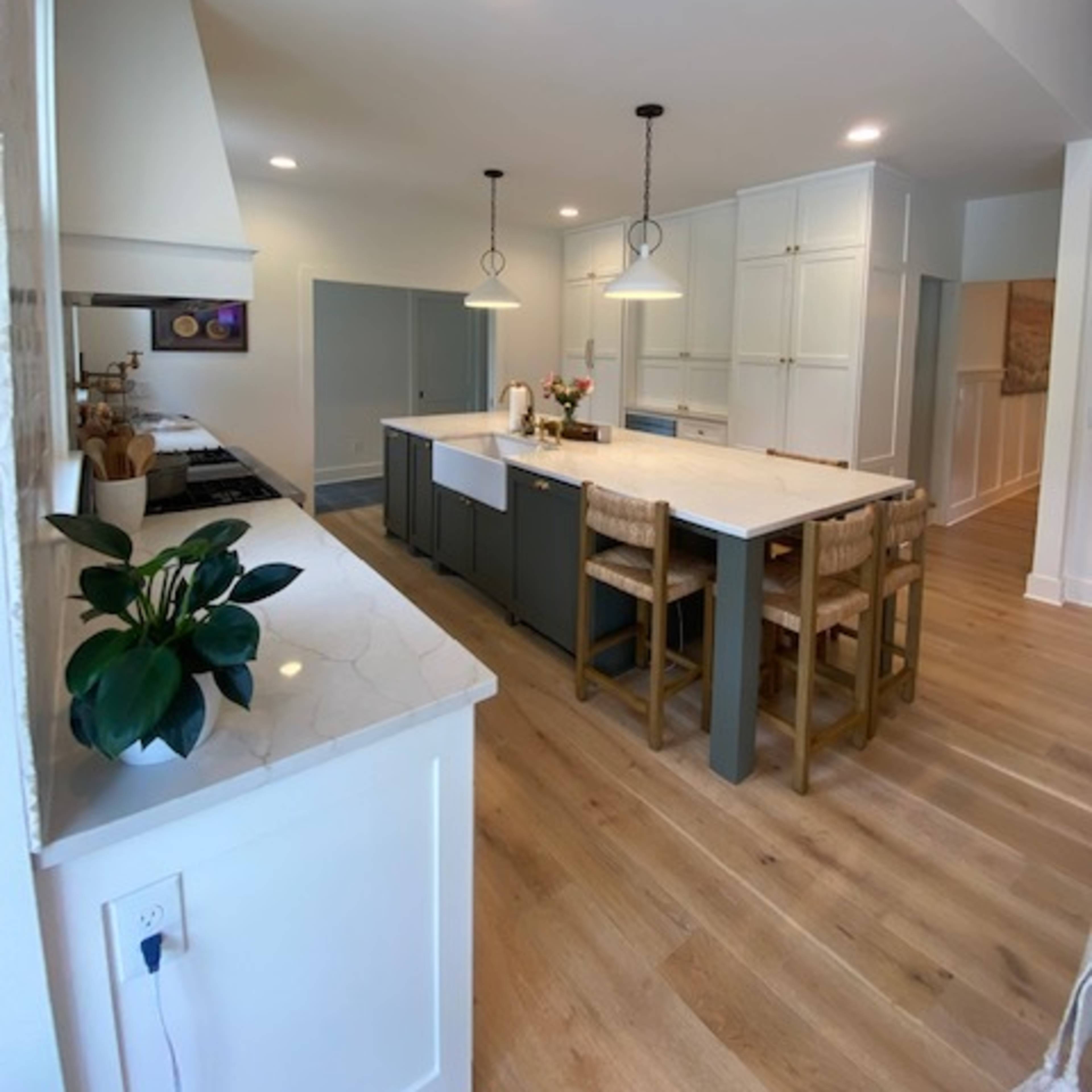 A modern kitchen with a central island, bar seating, and light-colored cabinetry set against wooden flooring.