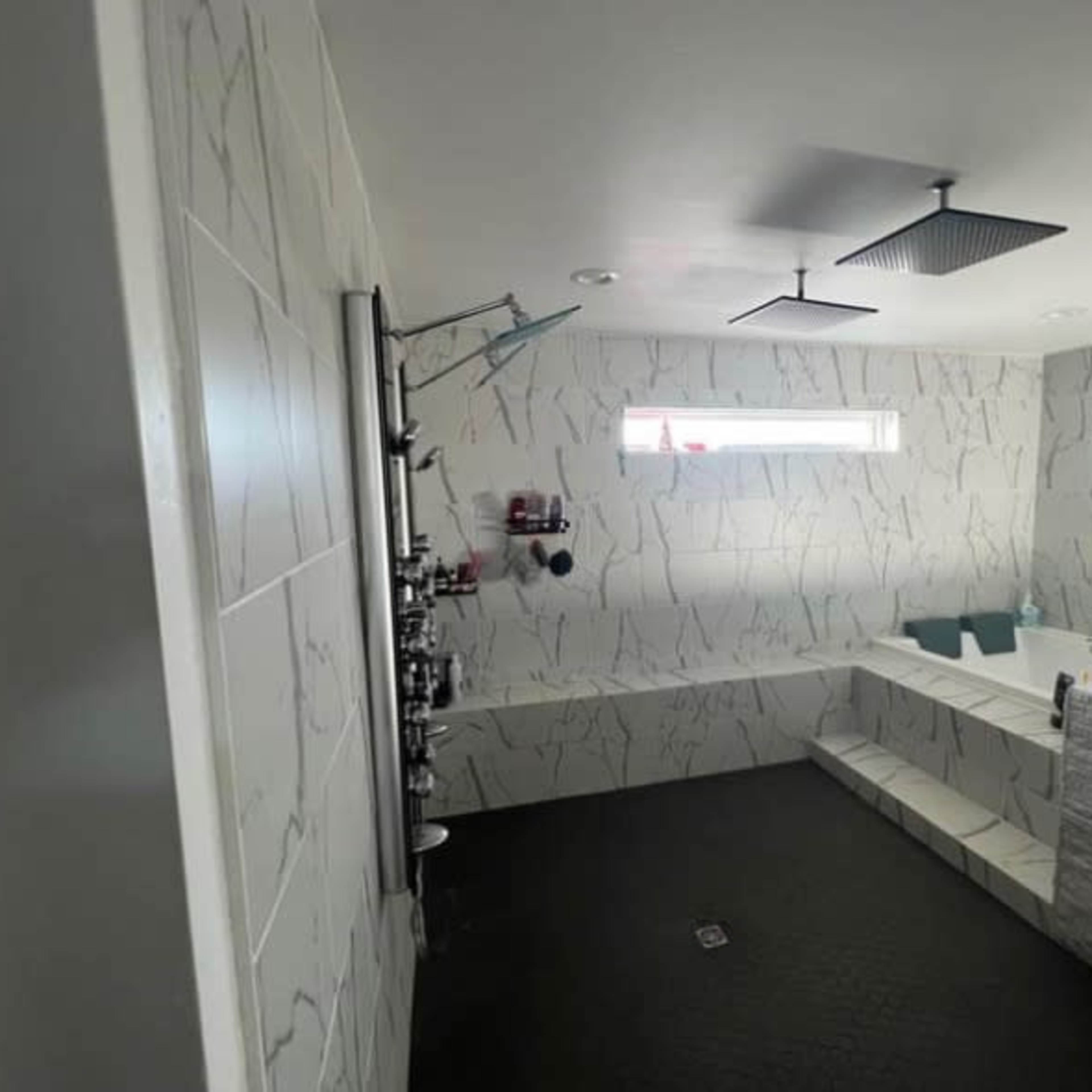A modern bathroom featuring a tub, a shower area, and walls covered in light-colored tile with a marble-like pattern.