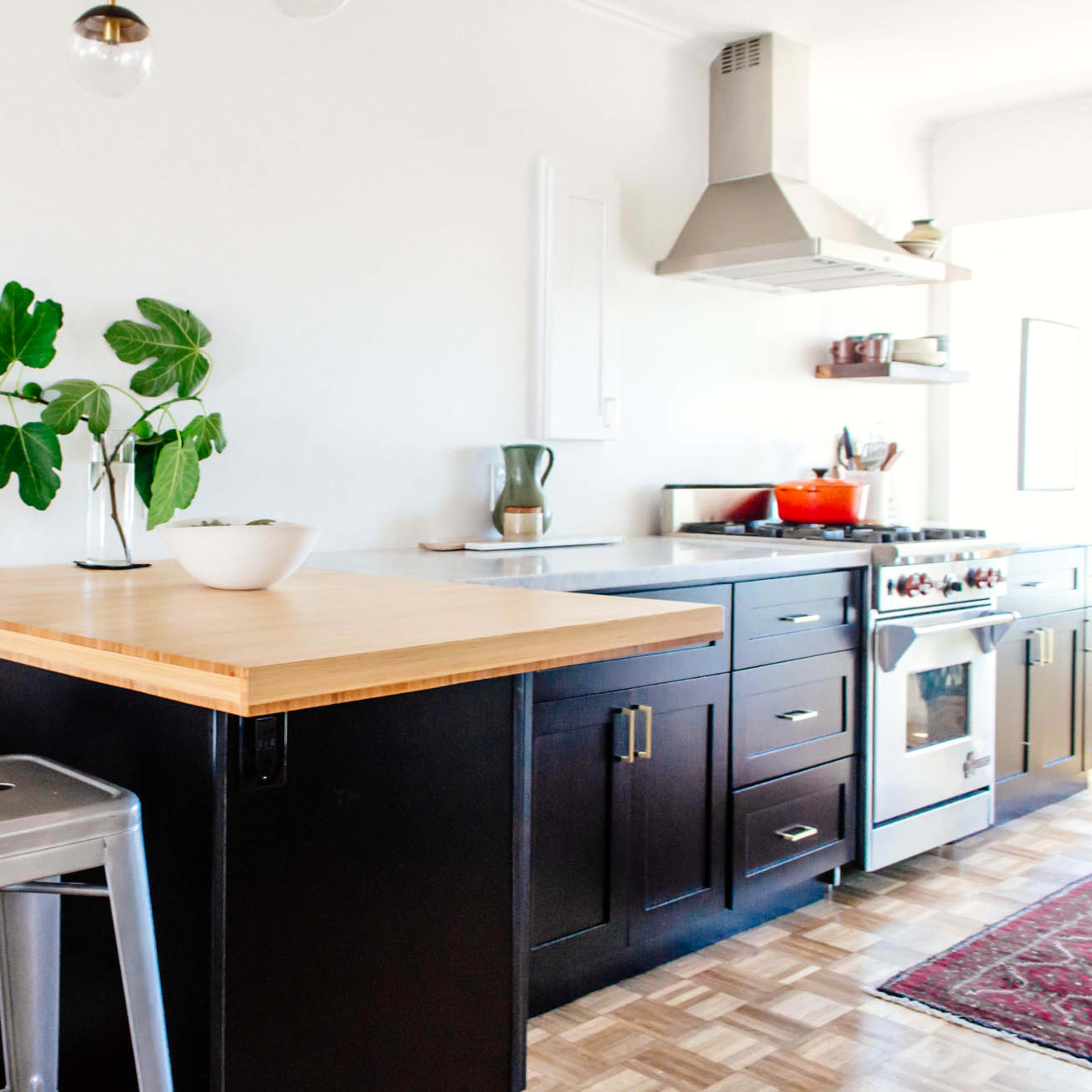 A modern kitchen with a wooden island, metal stools, and stainless steel appliances, including a stove and an exhaust hood.