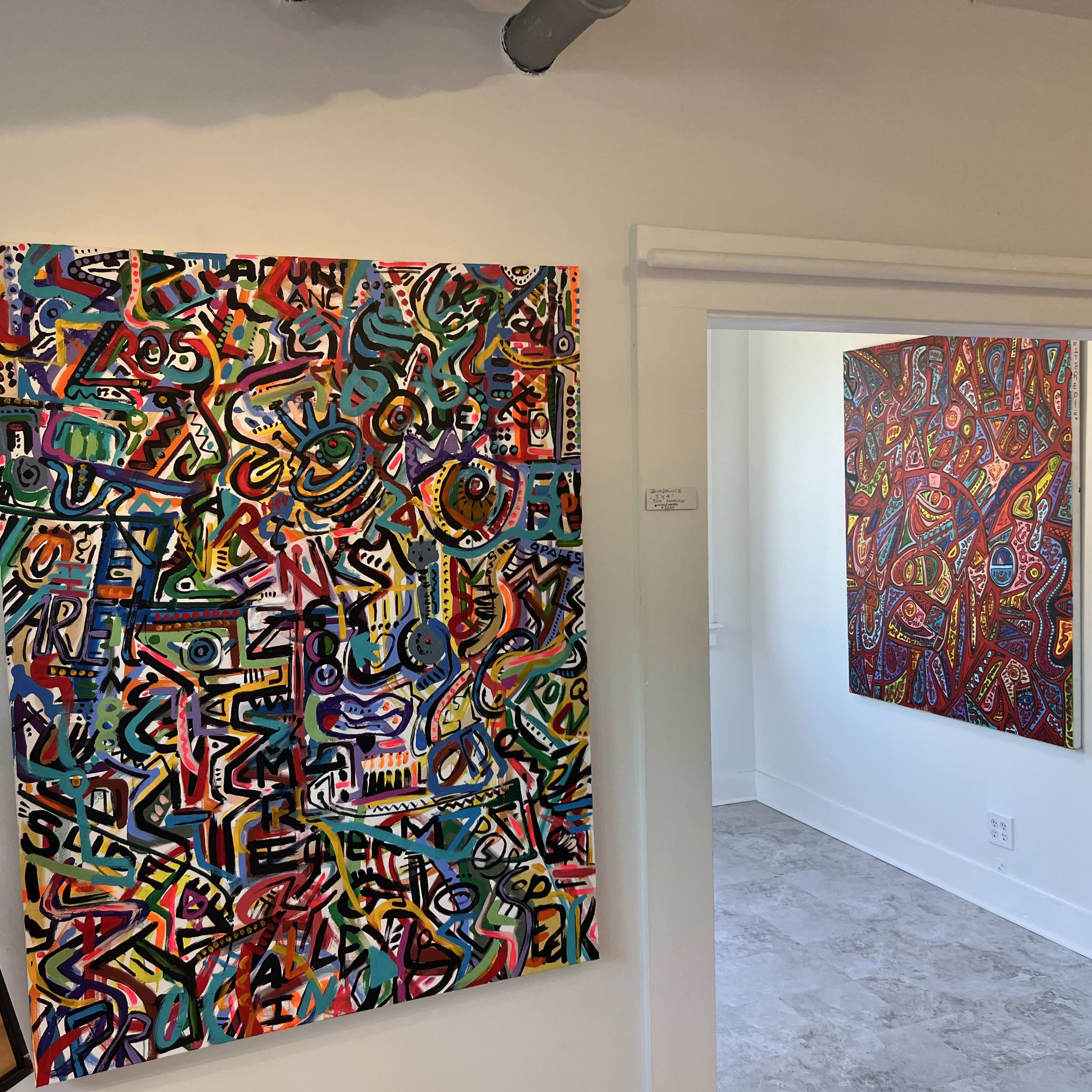 Two abstract paintings displayed on the walls of a bright room with light-colored flooring.