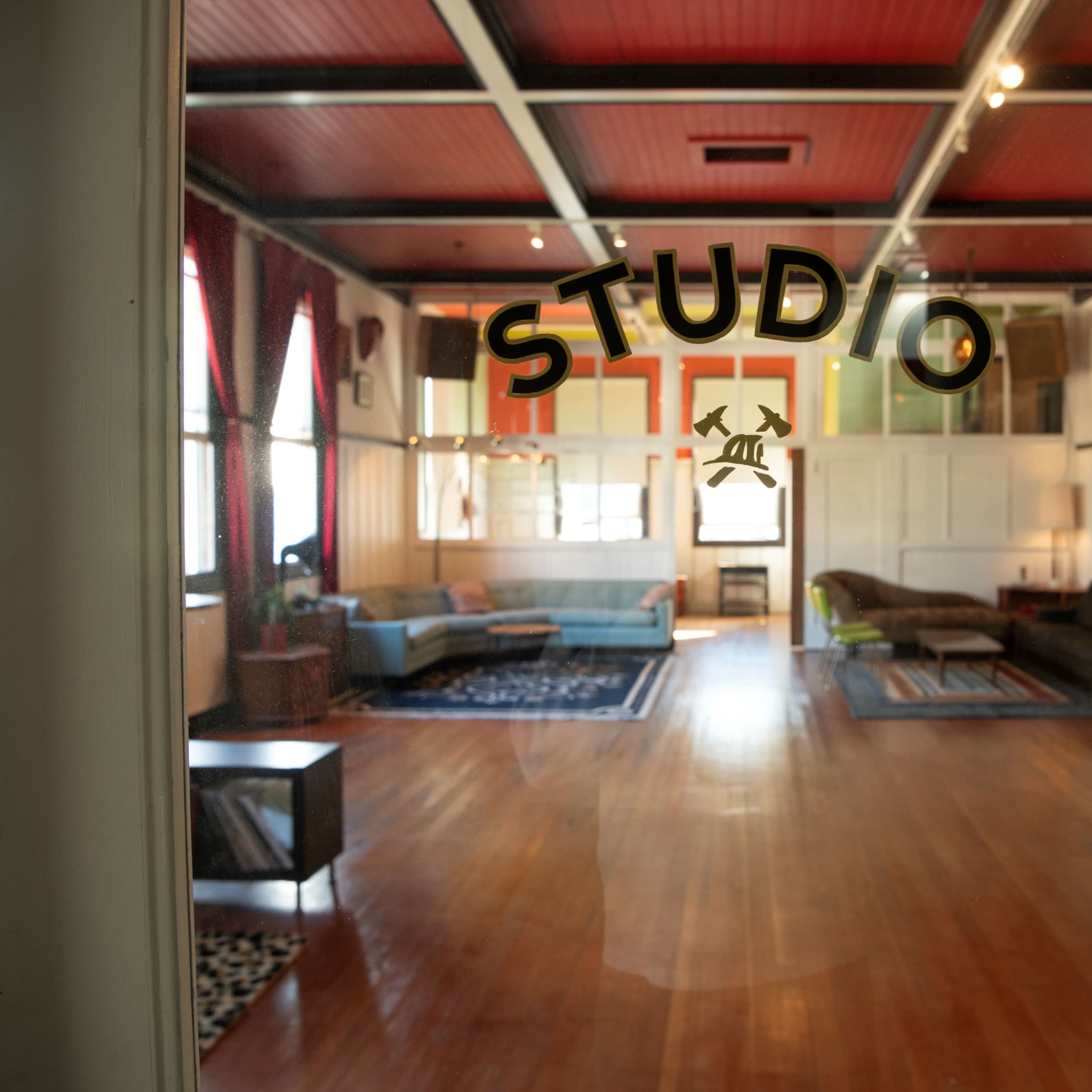A spacious studio with wooden floors, large windows, and various seating arrangements.