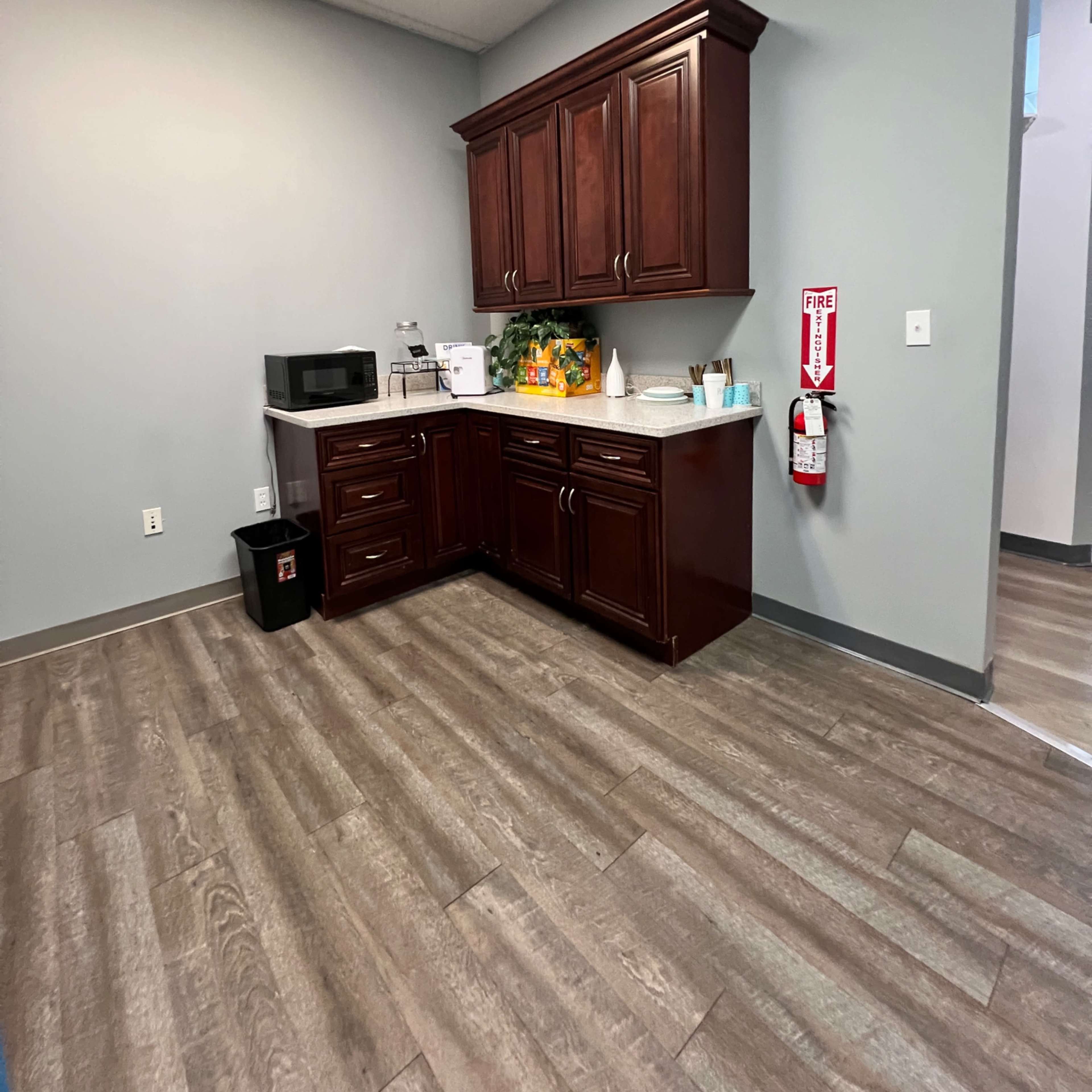 A kitchen area with dark wooden cabinets, a countertop, a microwave, and a fire extinguisher mounted on the wall.