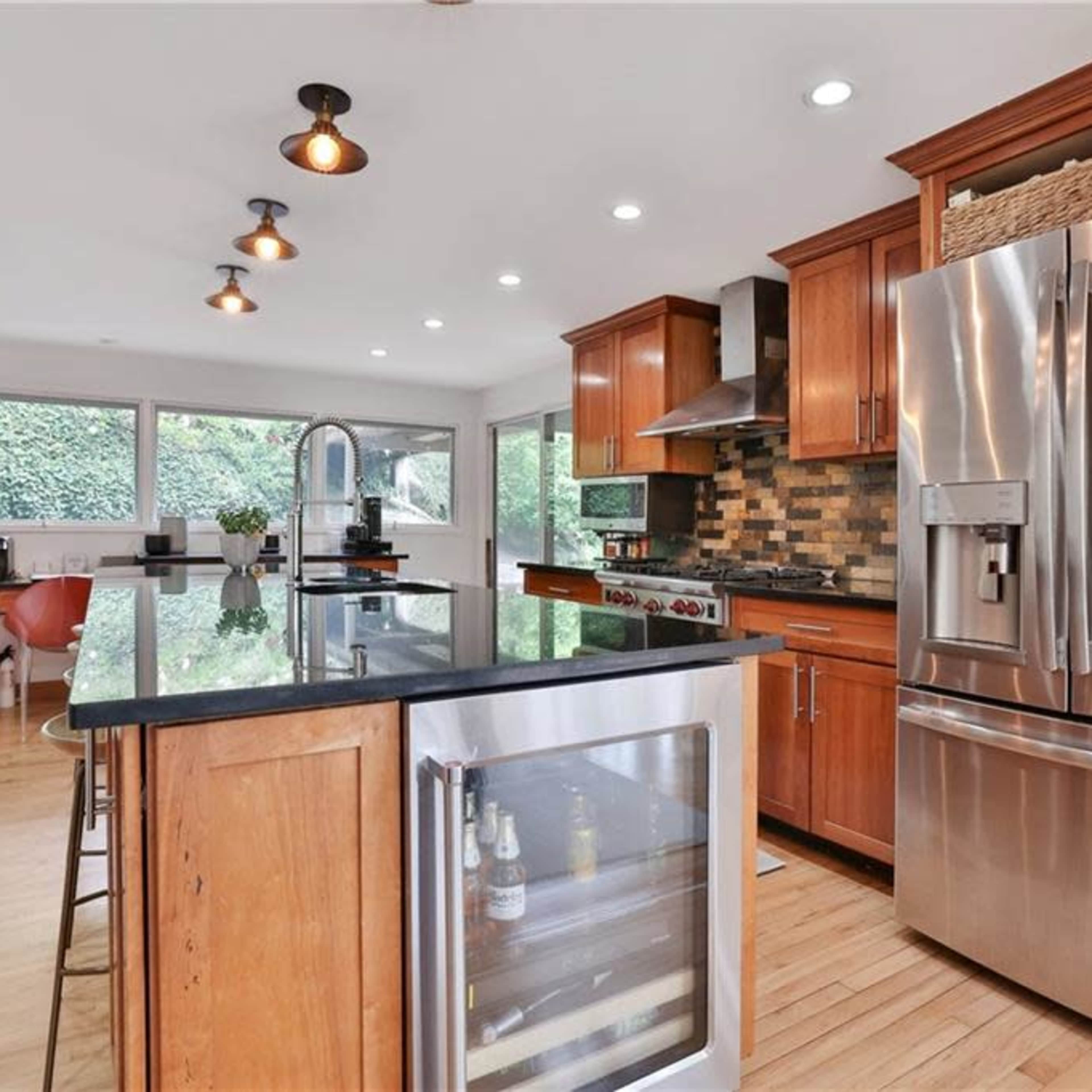 A modern kitchen with wooden cabinets, stainless steel appliances, an island with a granite countertop, and large windows letting in natural light.