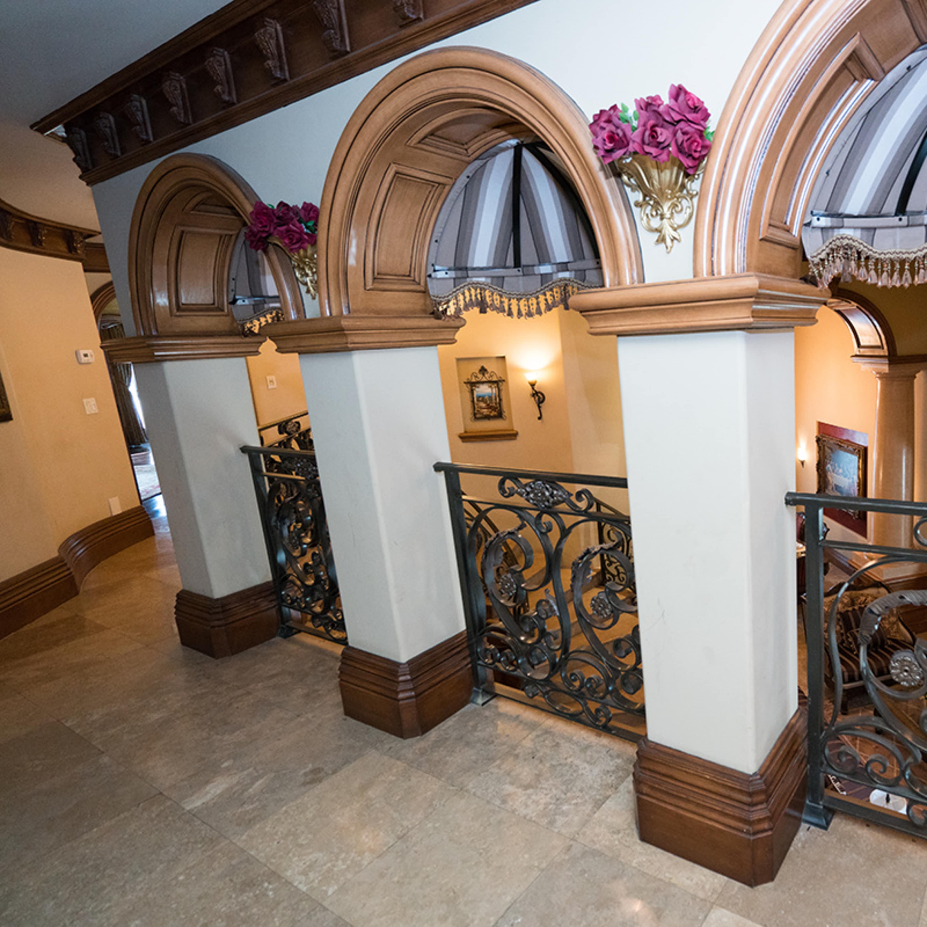 A hallway featuring ornate arches and a decorative railing overlooking a lower level with furniture and artwork.