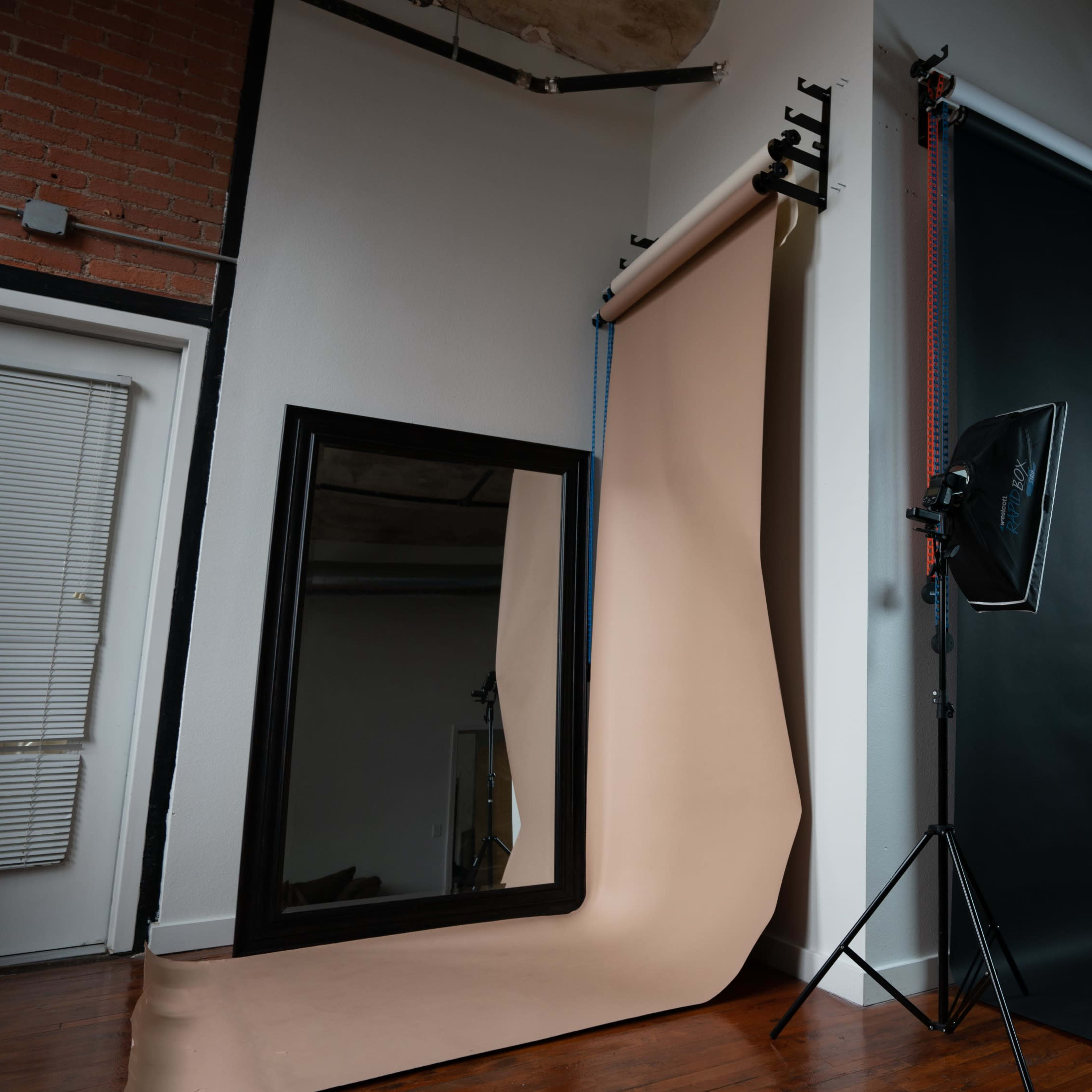 A photography studio with a large mirror, a beige backdrop, a black backdrop, a lighting setup, and a stool.