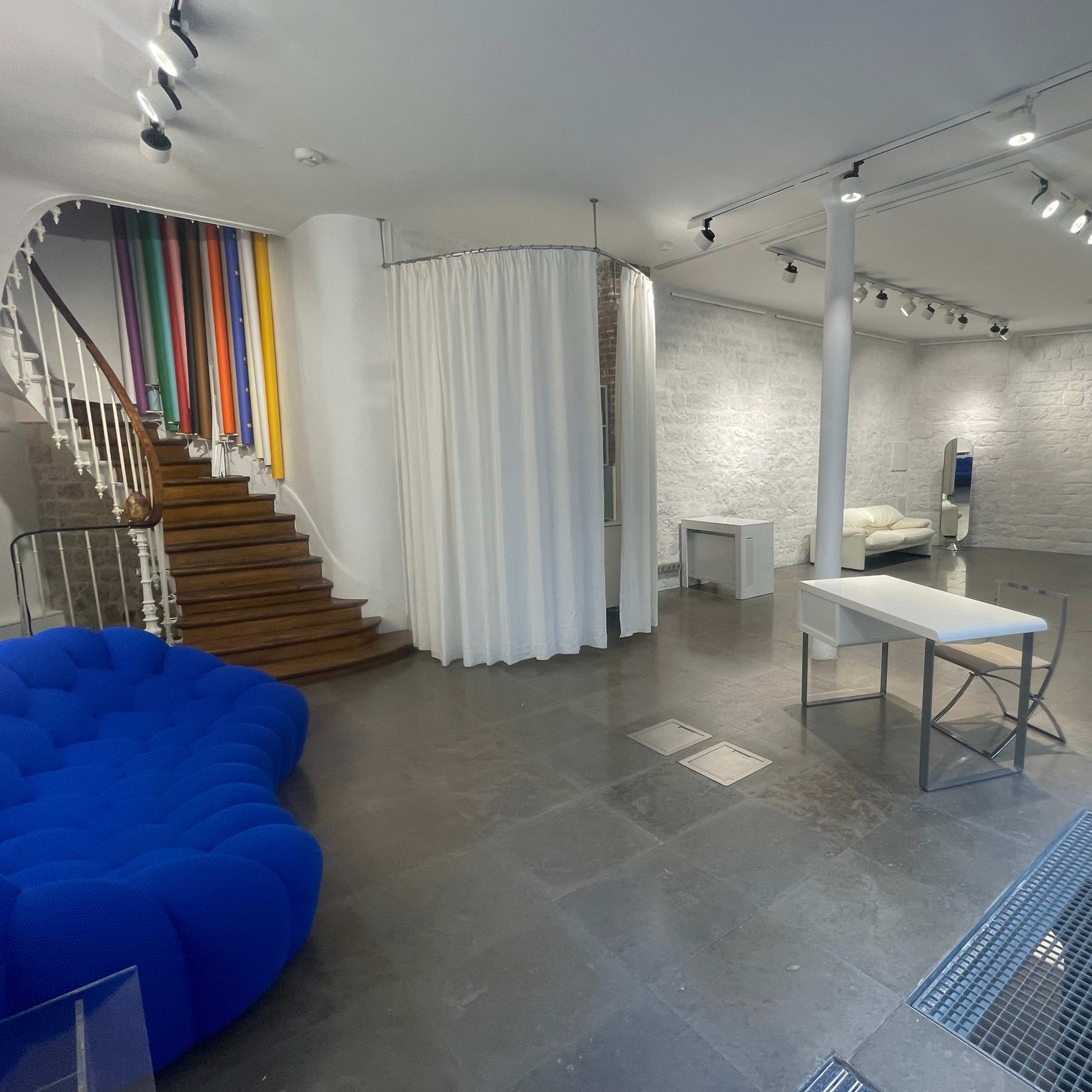 A spacious room with a blue couch, a white table, and colorful dividers leading up a staircase.