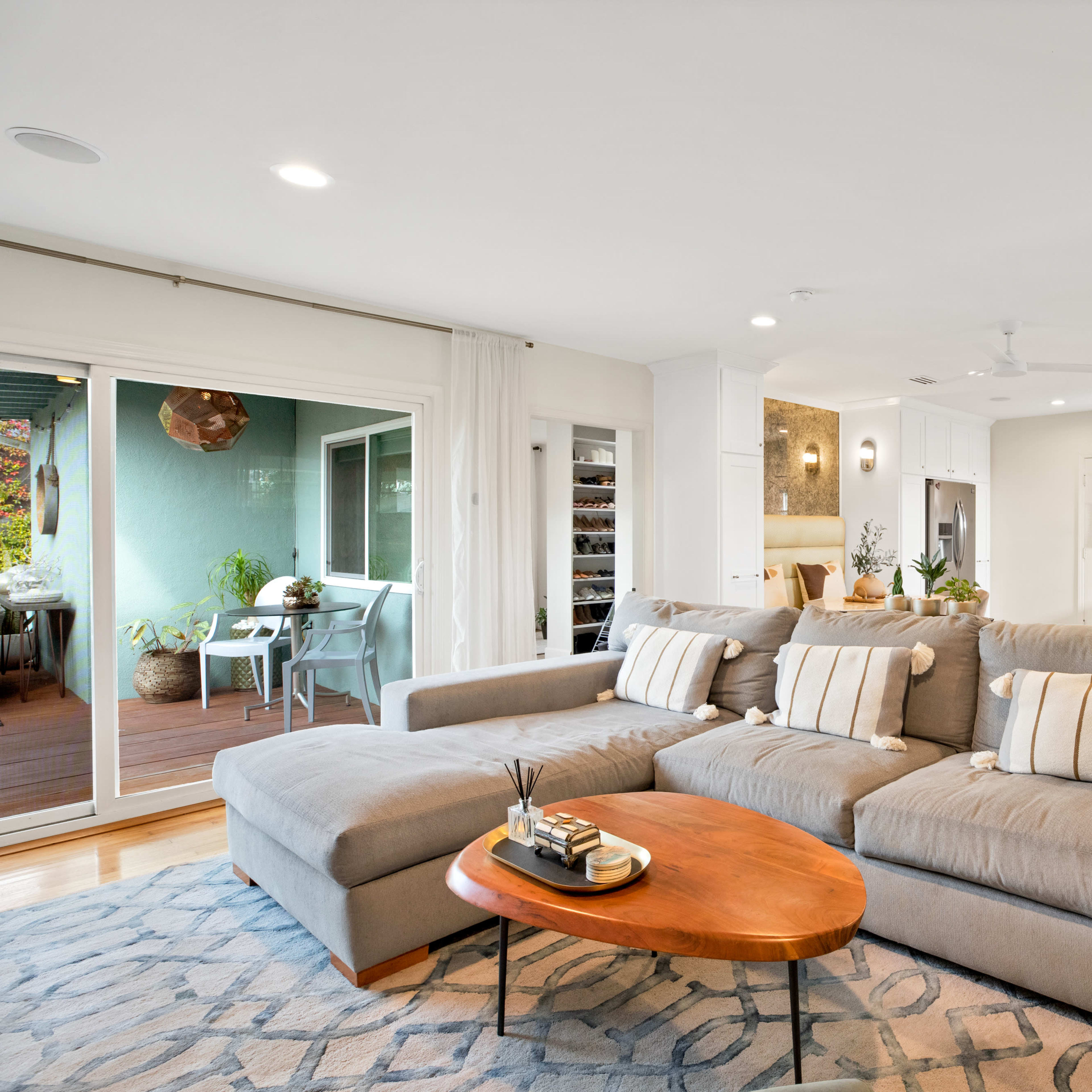 A modern living room features a gray sectional sofa, a wooden coffee table, and an open layout leading to a kitchen and dining area.