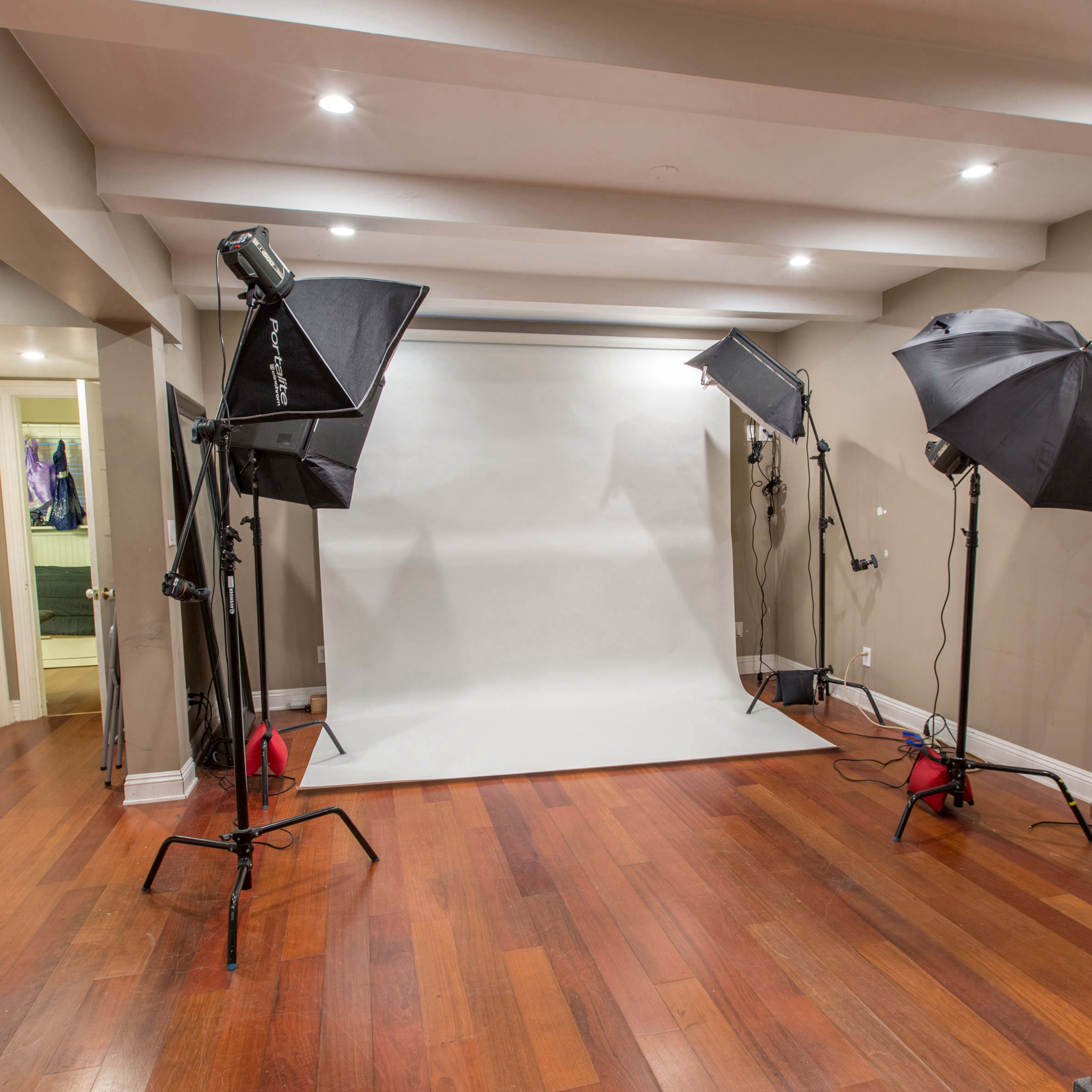 A photography studio with a blank backdrop and three light stands set up on a wooden floor.