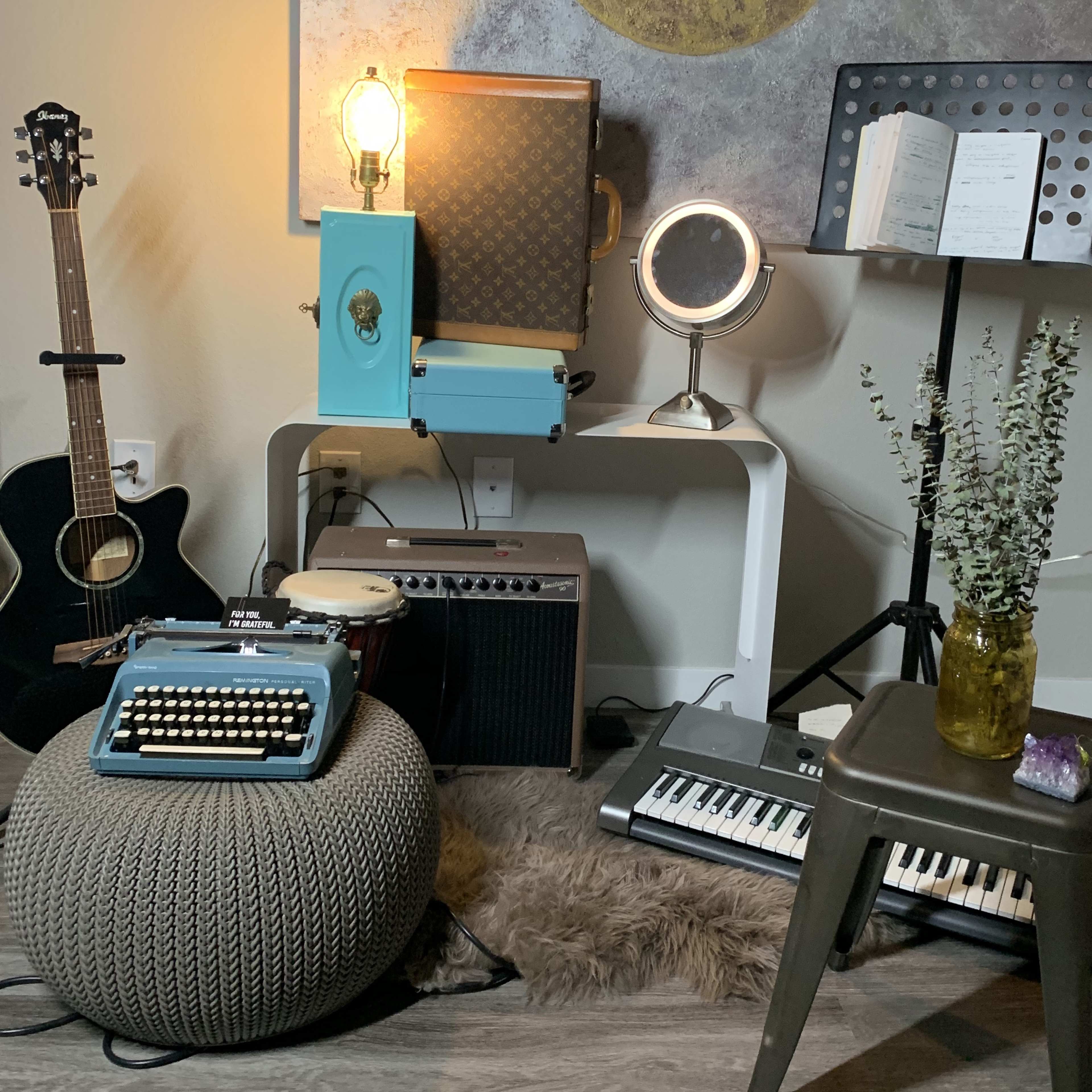 A cozy corner includes a guitar, vintage typewriter, amplifier, keyboard, and decorative elements arranged around a pouf and side table.