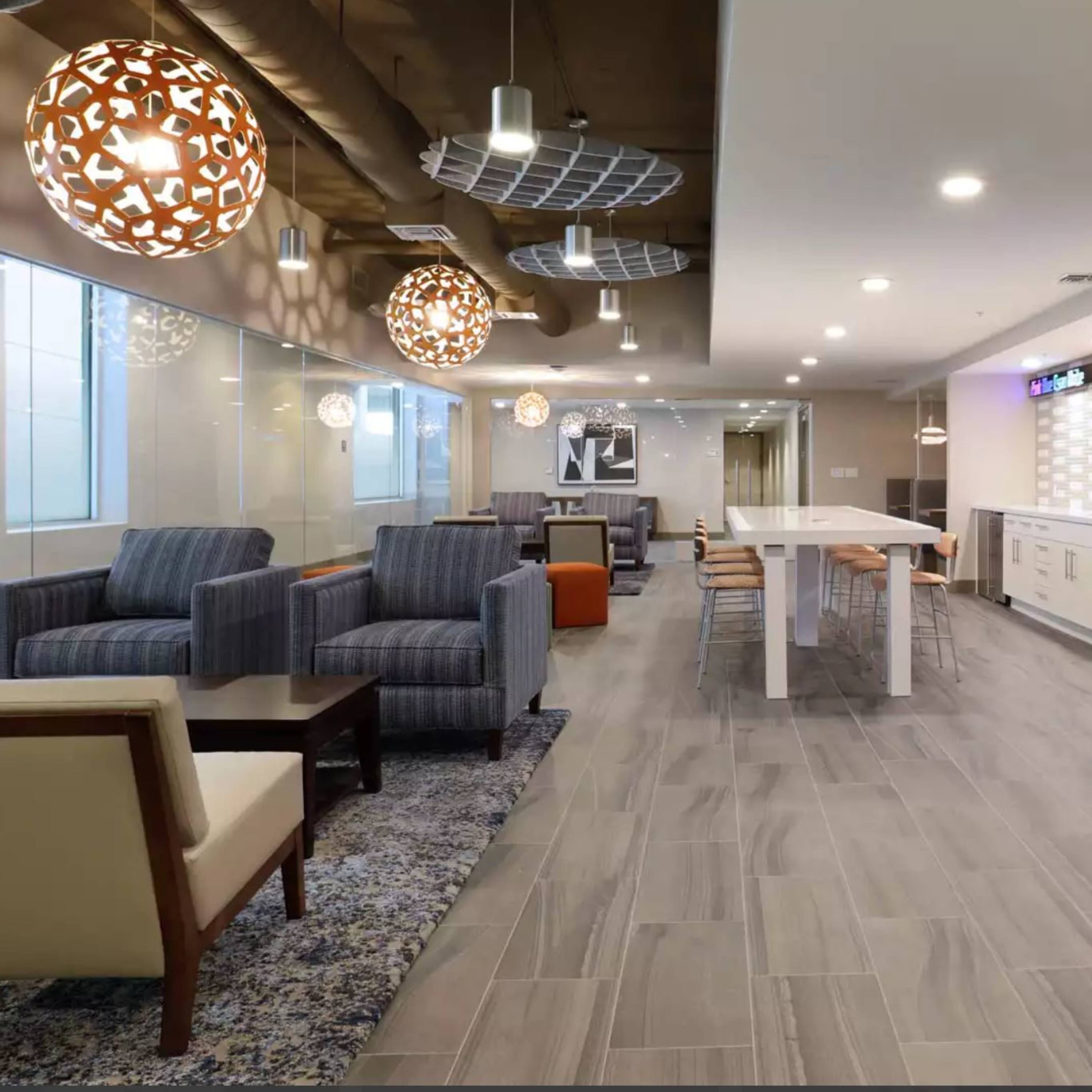 A modern lounge area with seating arrangements, pendant lights, and a kitchenette along one wall.