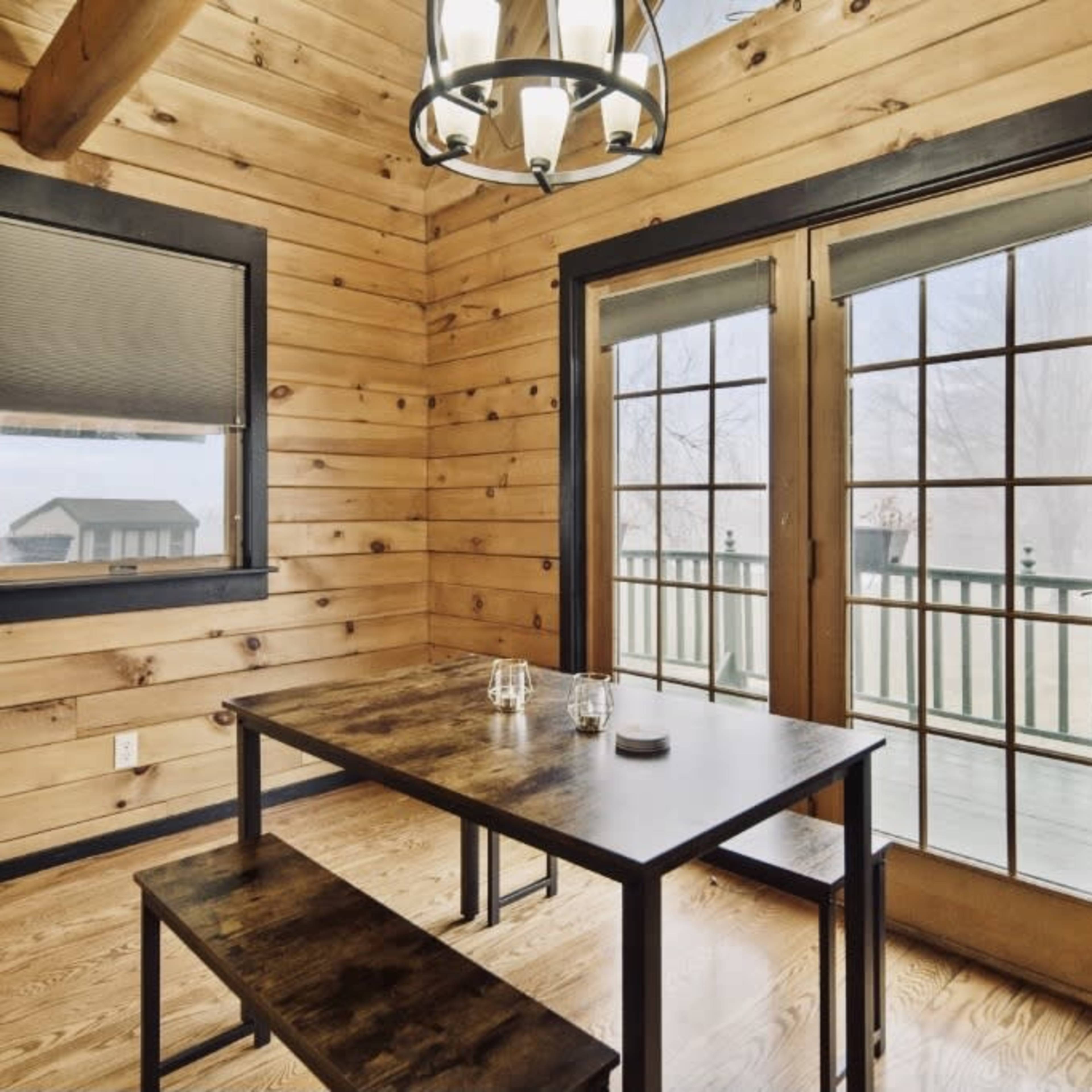 A dining area features a wooden table and benches, with large double doors opening to a deck and wooden paneled walls.