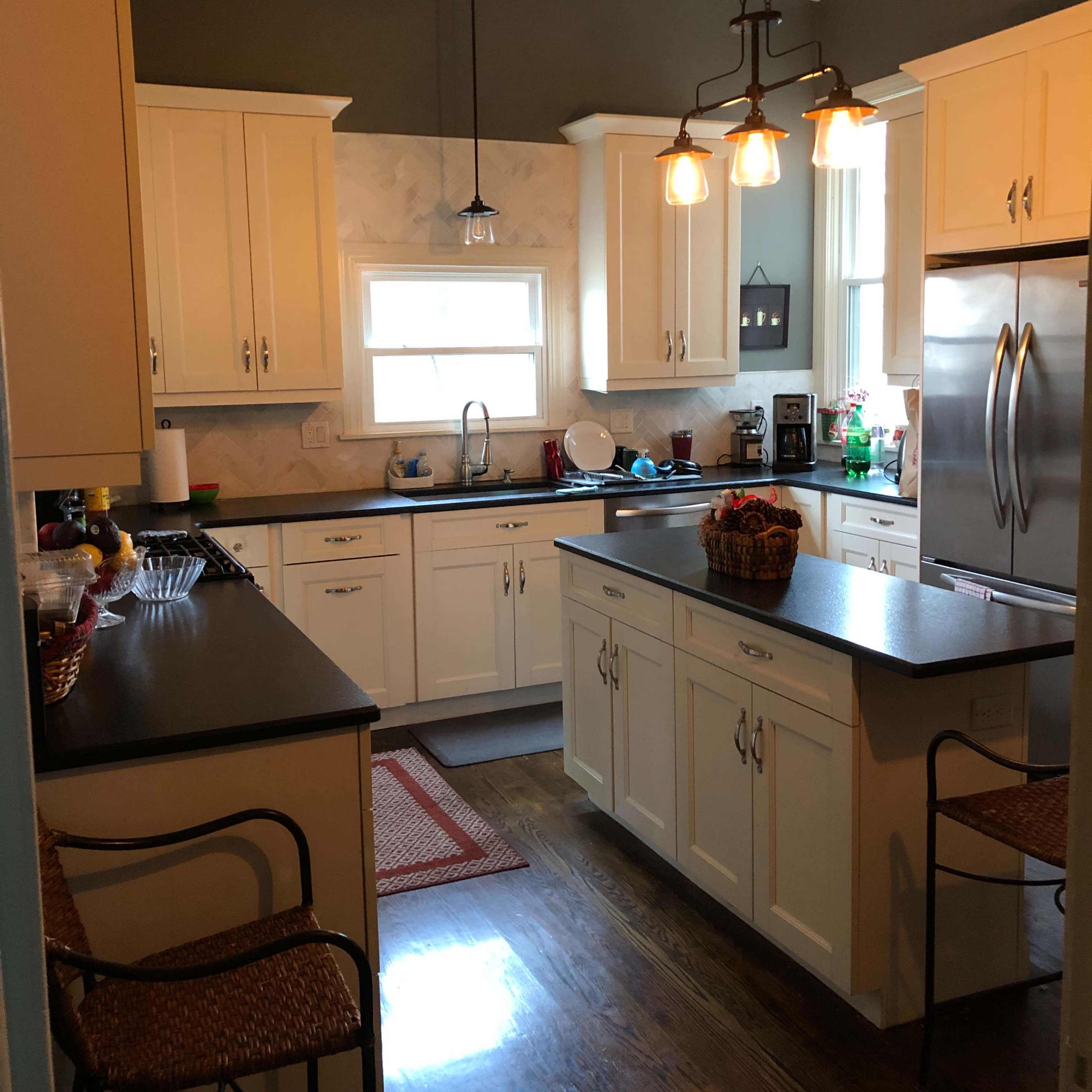 A modern kitchen with white cabinets, a central island, and warm lighting fixtures.