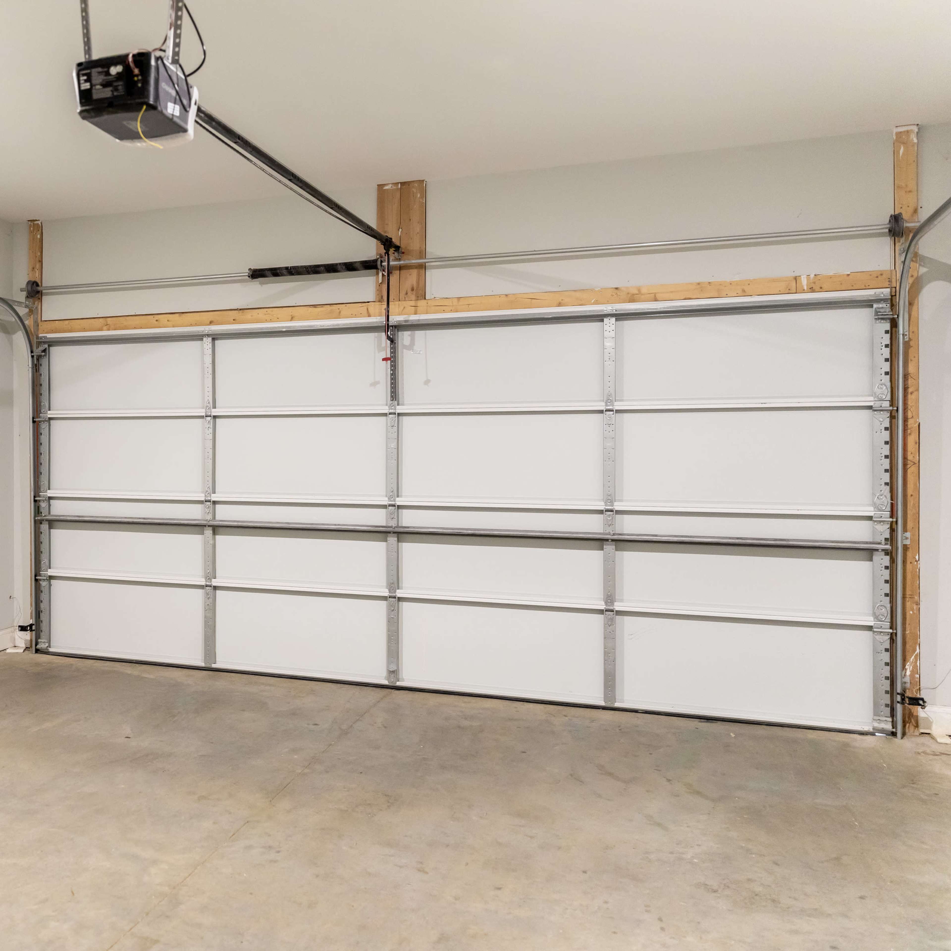 A clean, empty garage with a large, closed sectional door and bare concrete flooring.