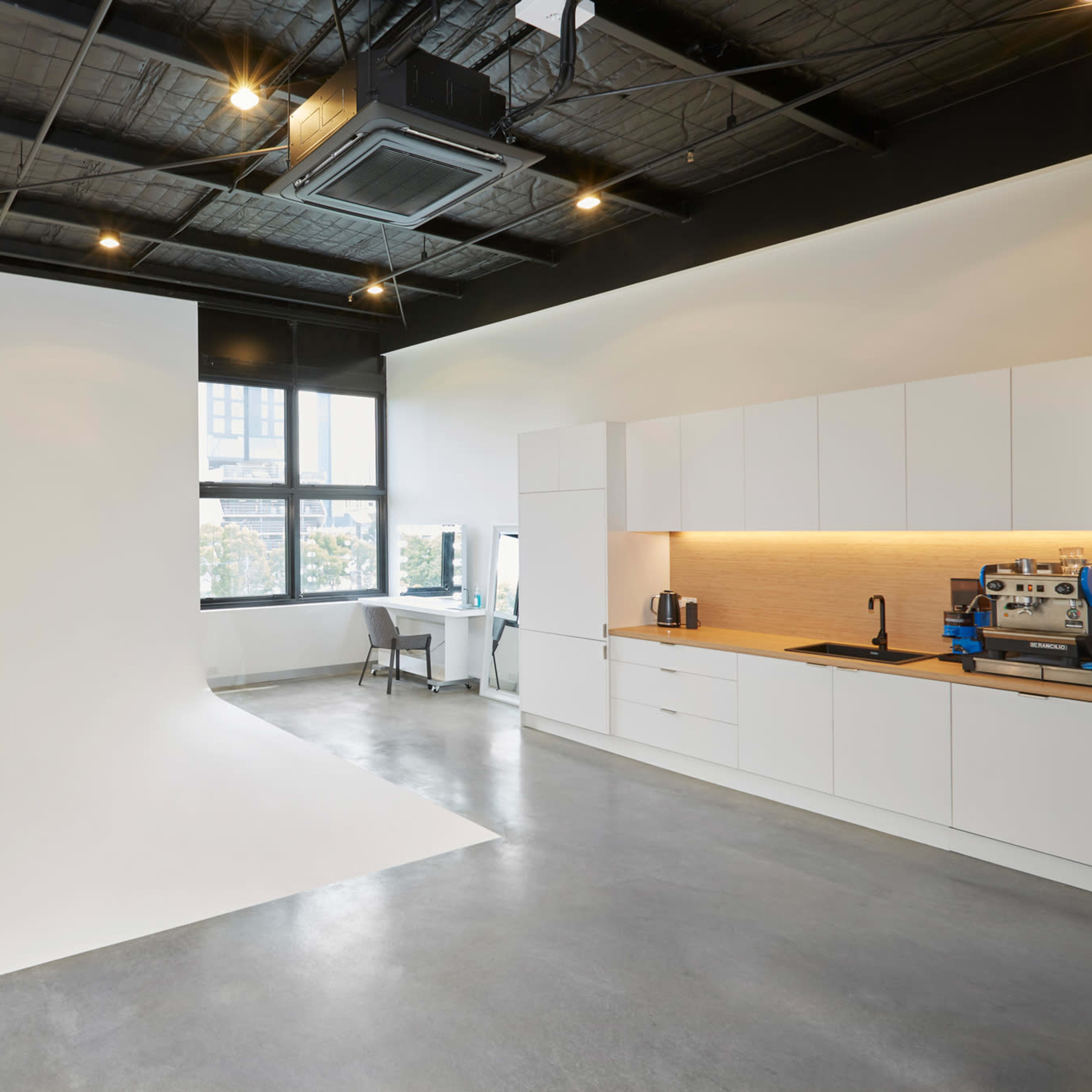 A bright studio space with a seamless white backdrop on one side and a modern kitchen area with cabinetry and appliances on the other.