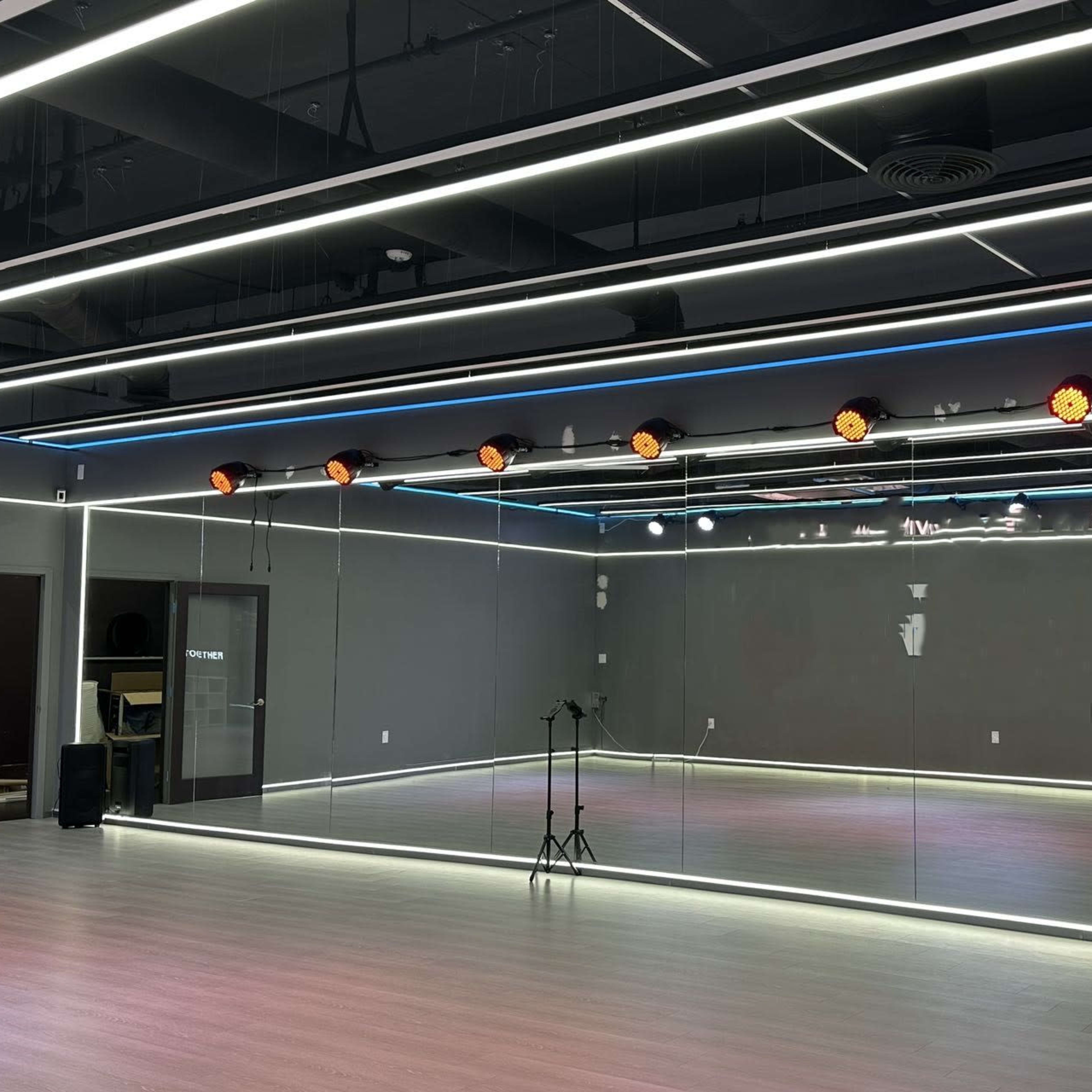 A spacious dance studio features large mirrors, sleek lighting, and a polished wooden floor.