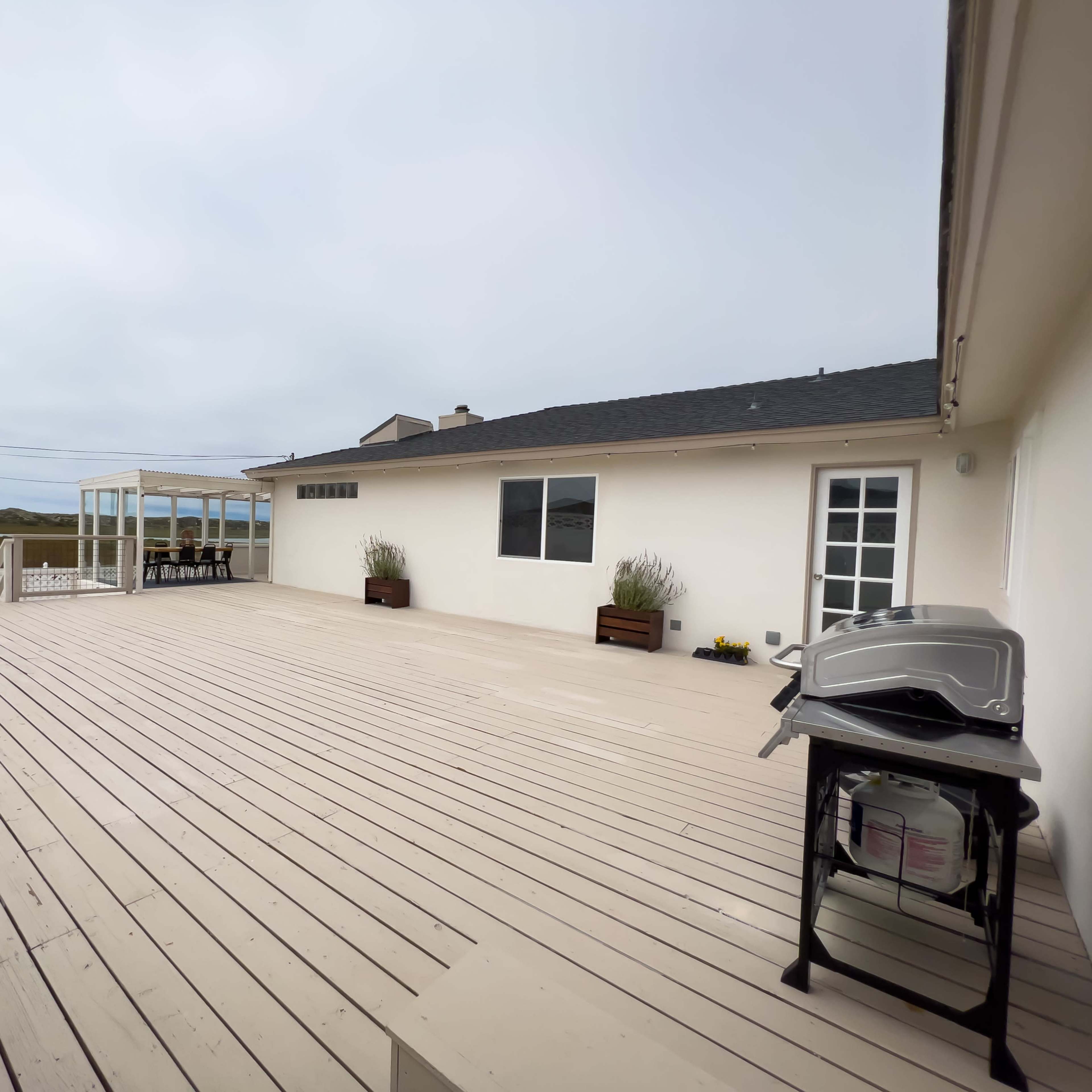 A spacious wooden deck connected to a house, with a barbecue grill and seating area visible under a cloudy sky.