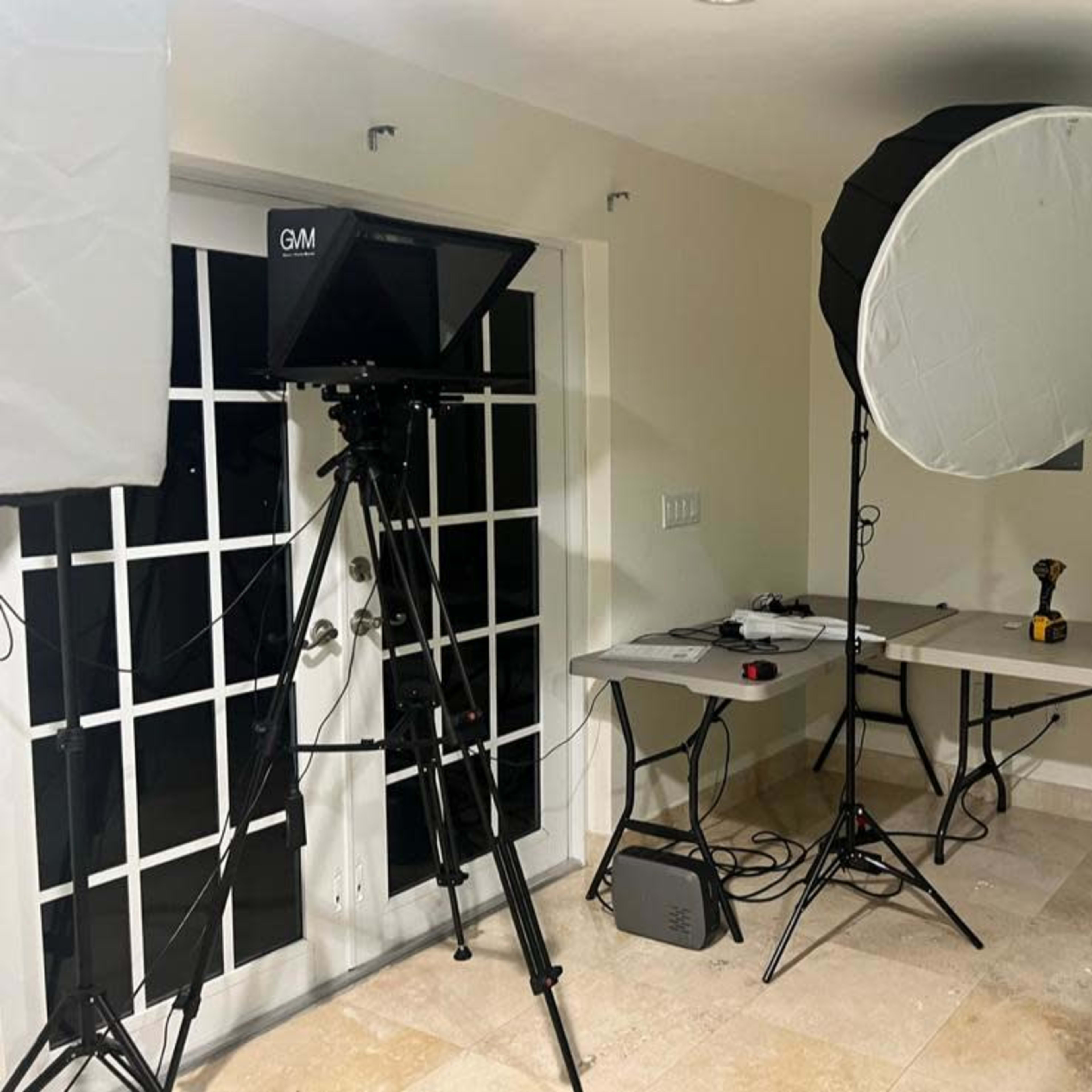 A well-lit indoor studio setup with a camera on a tripod, a large softbox light, and several tables with equipment.