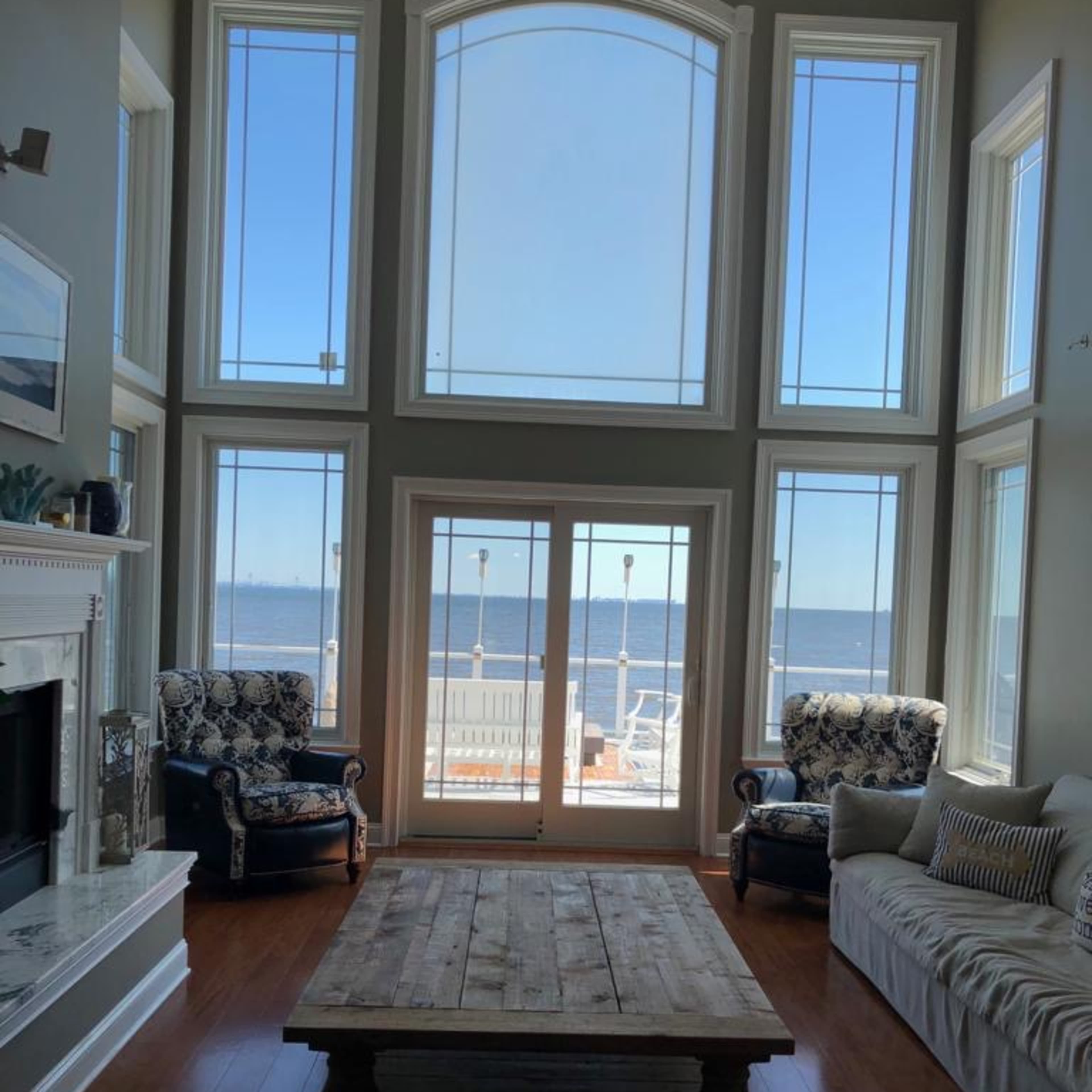 A living room with large windows overlooking a body of water, featuring two armchairs and a wooden coffee table.