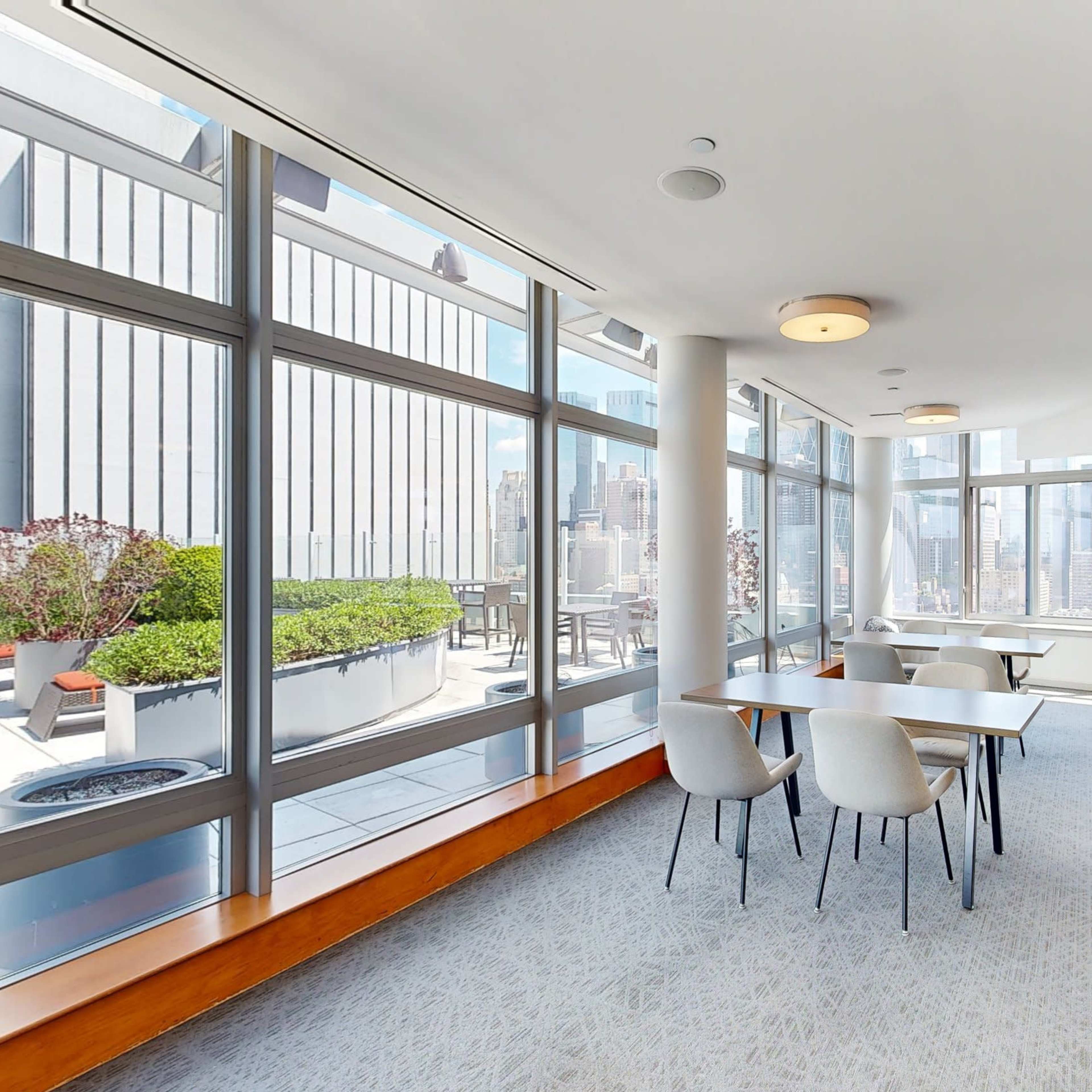 A bright, modern lounge area with large windows and a mix of seating arrangements, overlooking a city skyline.