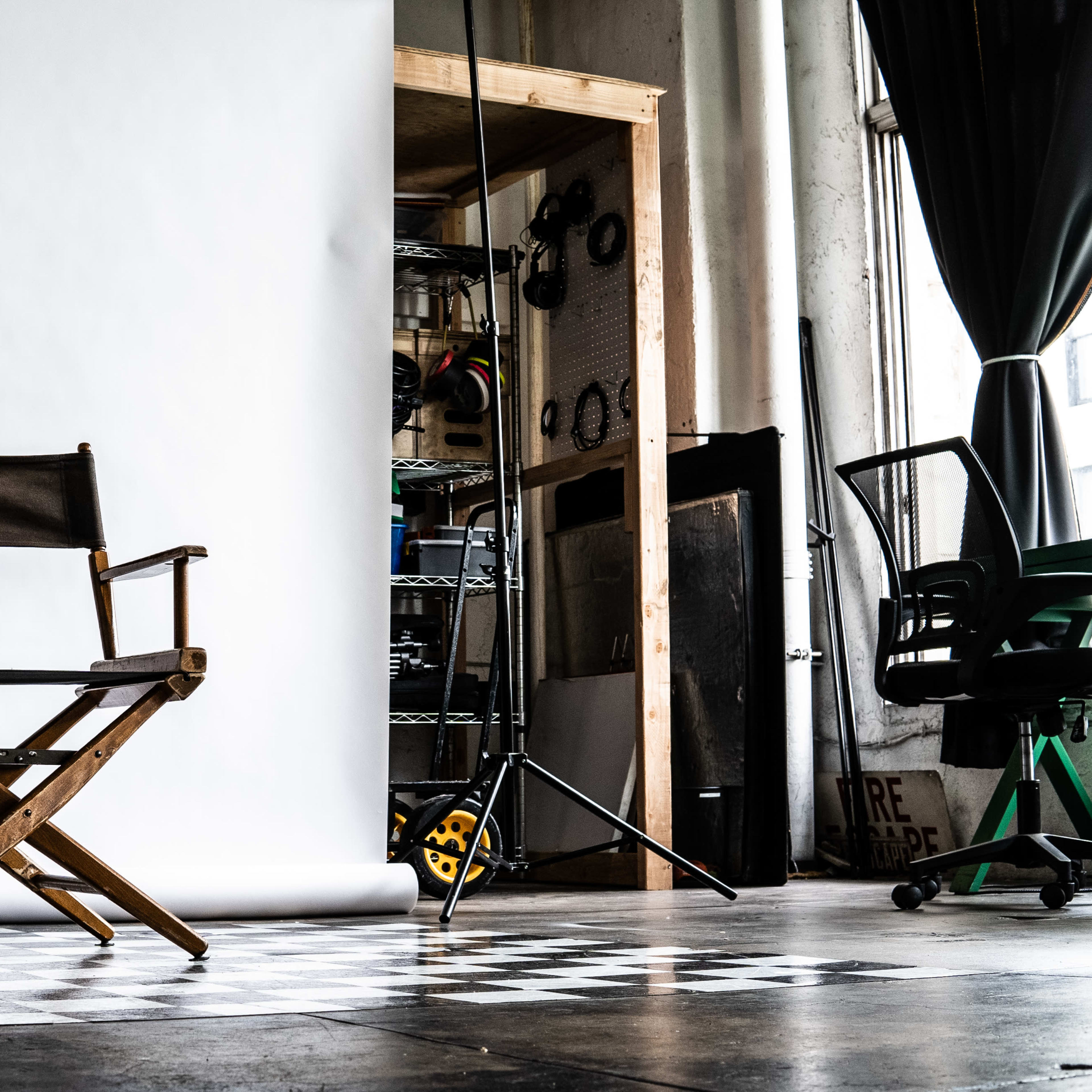 A wooden director's chair is positioned in front of a large white backdrop in a studio with shelves and equipment in the background.