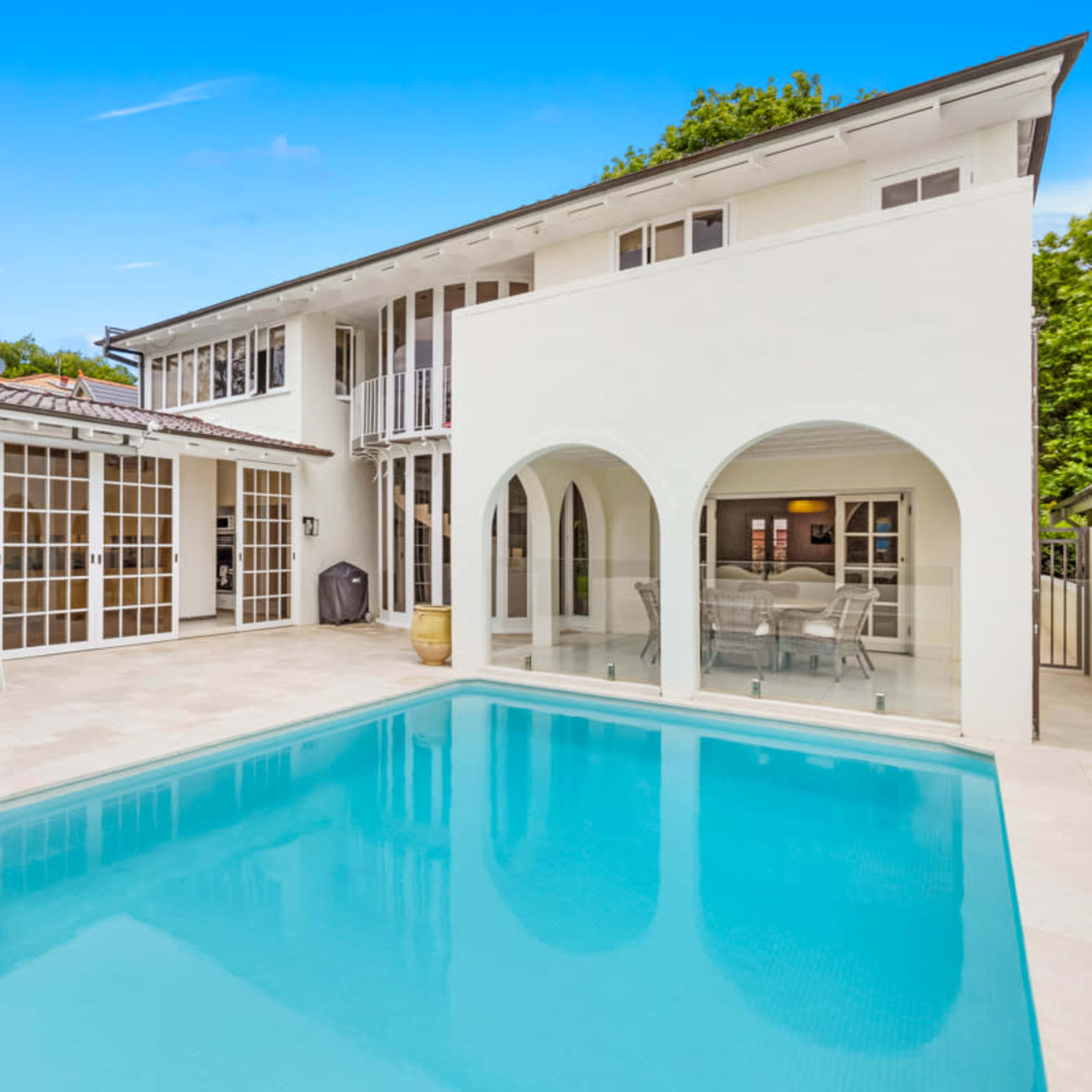 A clean, modern pool area features a clear blue swimming pool surrounded by tiled flooring and an outdoor seating arrangement.