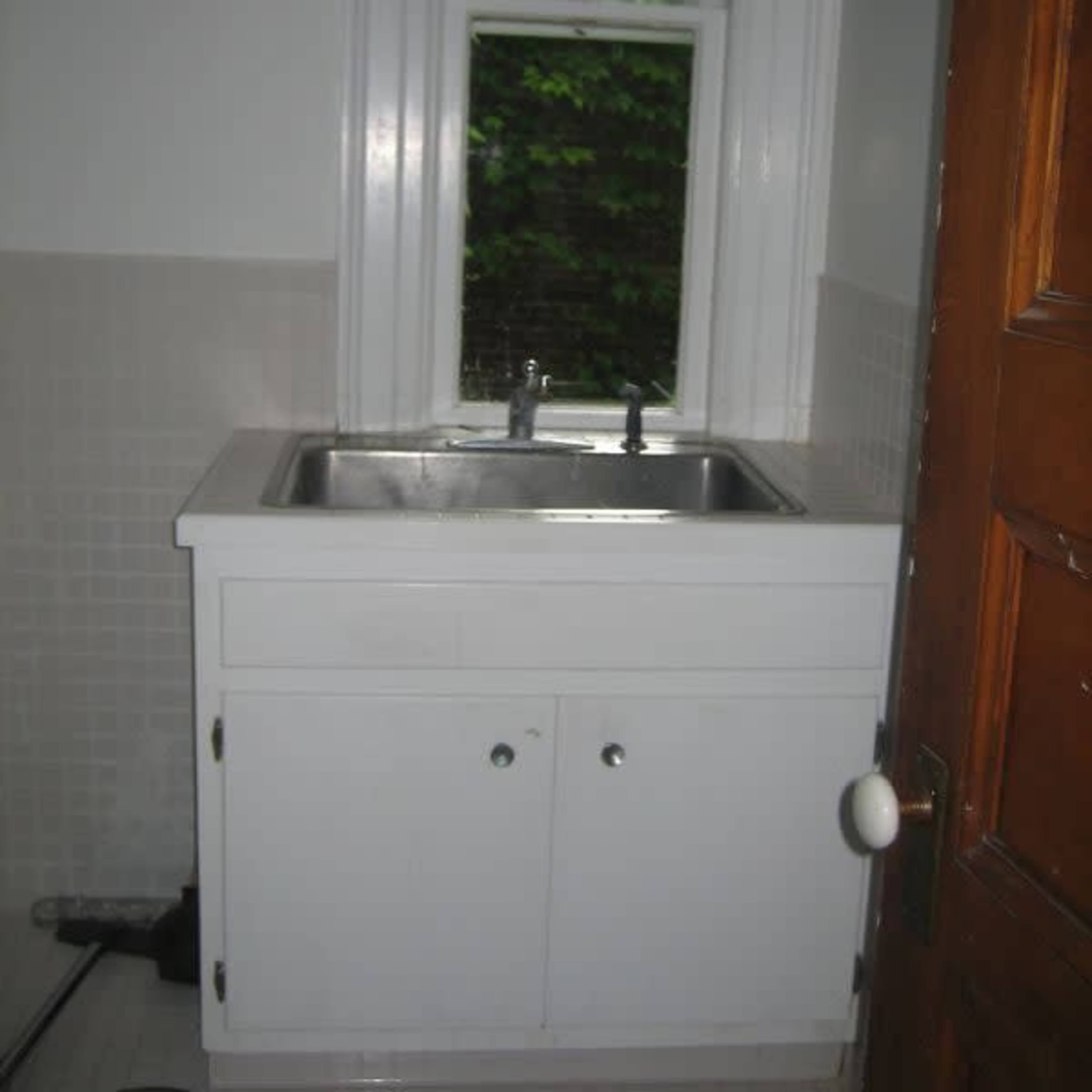 A white sink cabinet with a double basin, positioned against a wall next to a wooden door and a window.