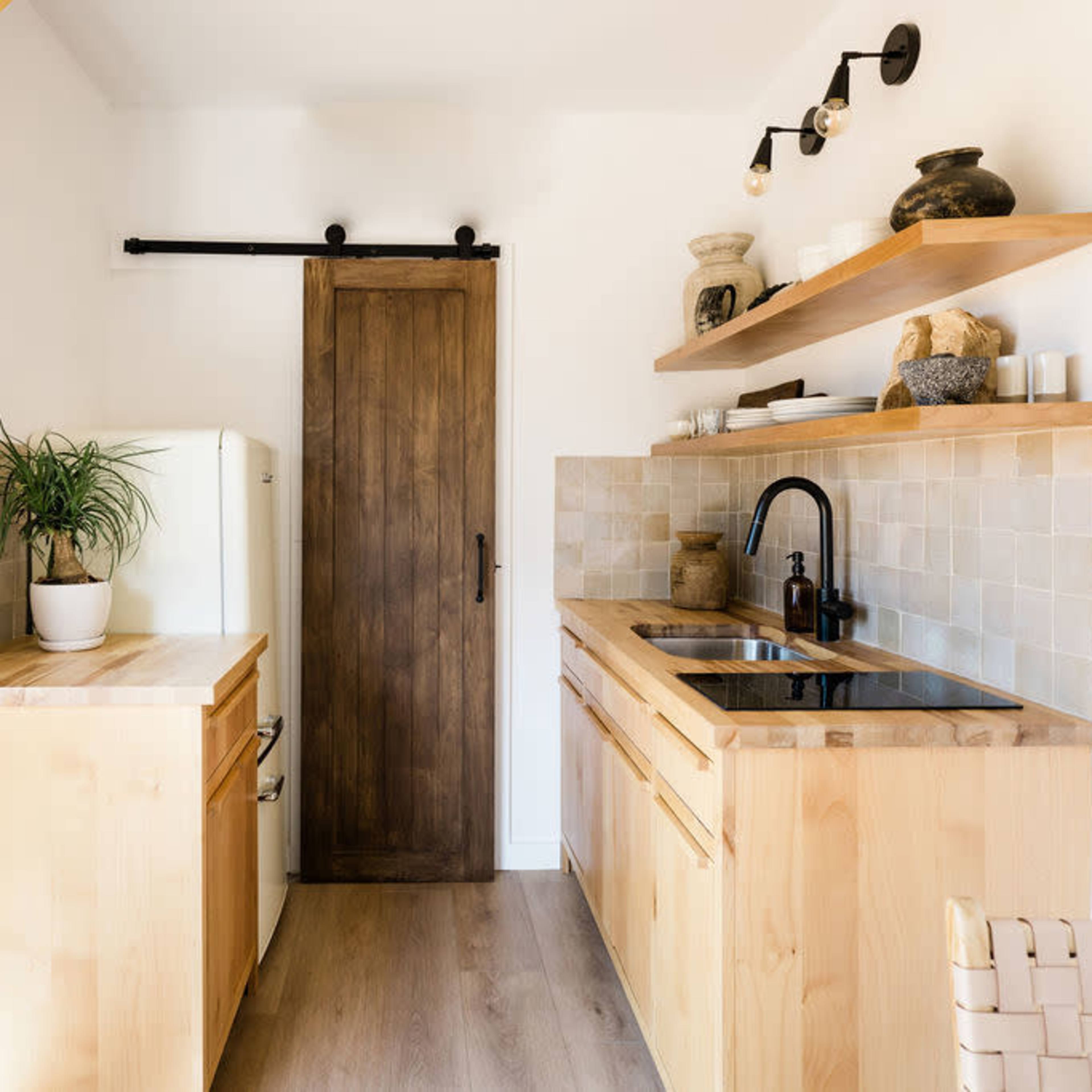 A bright kitchen with light wood cabinets, a sink, and a door leading to another area.