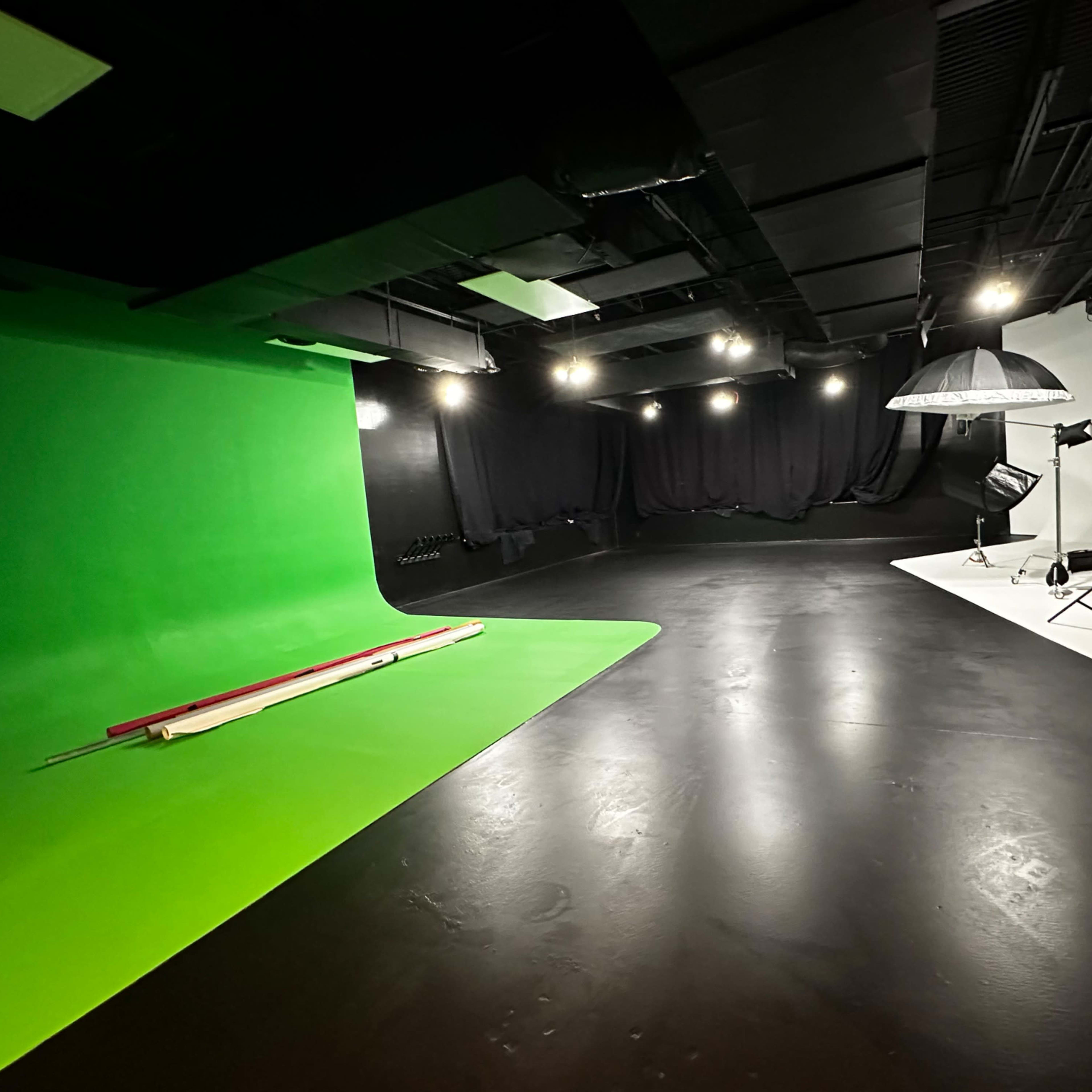 A studio space divided into two sections: one with a green screen and the other with a white backdrop, equipped with lighting and photography equipment.