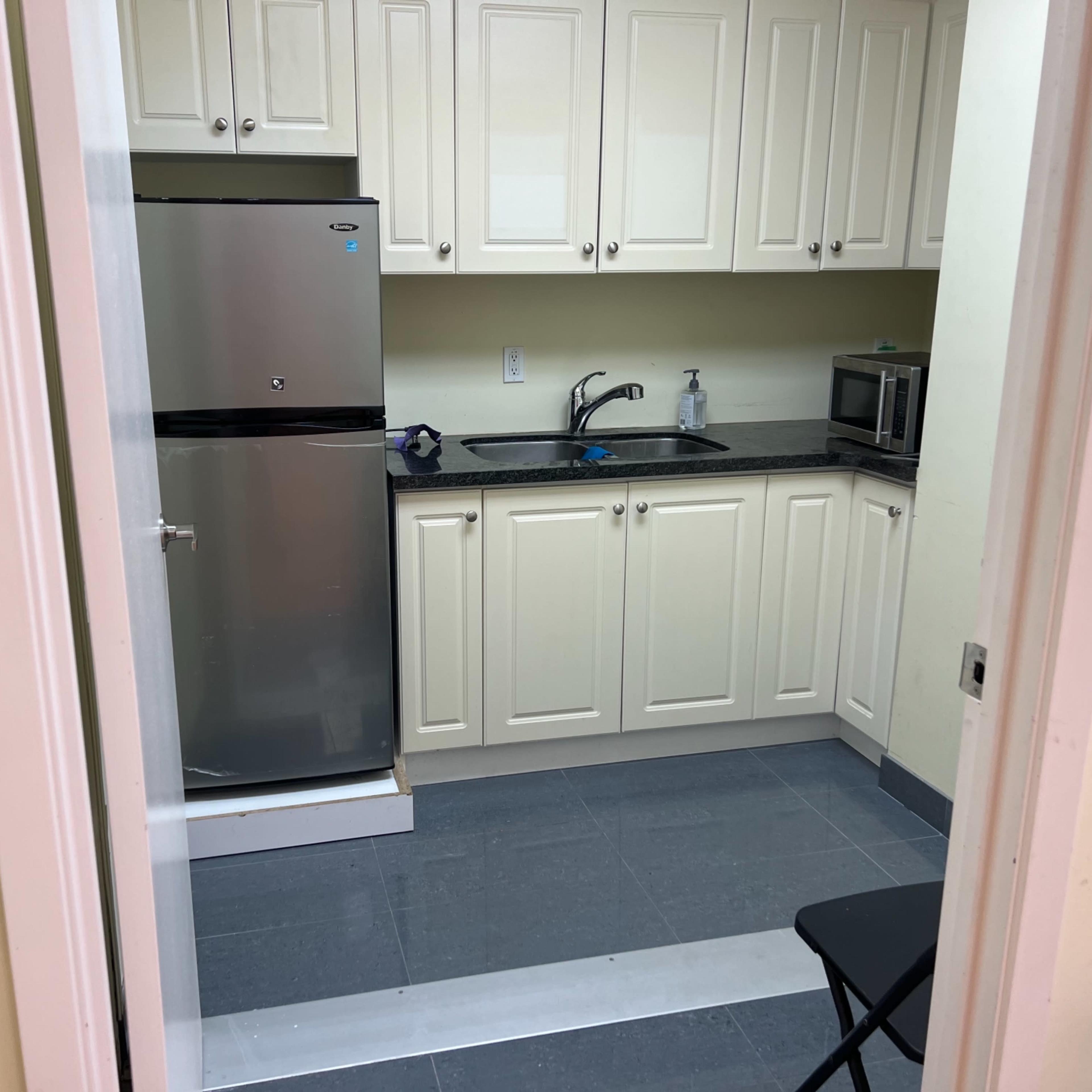 A small kitchen area featuring a refrigerator, sink, microwave, and cabinetry against light-colored walls.