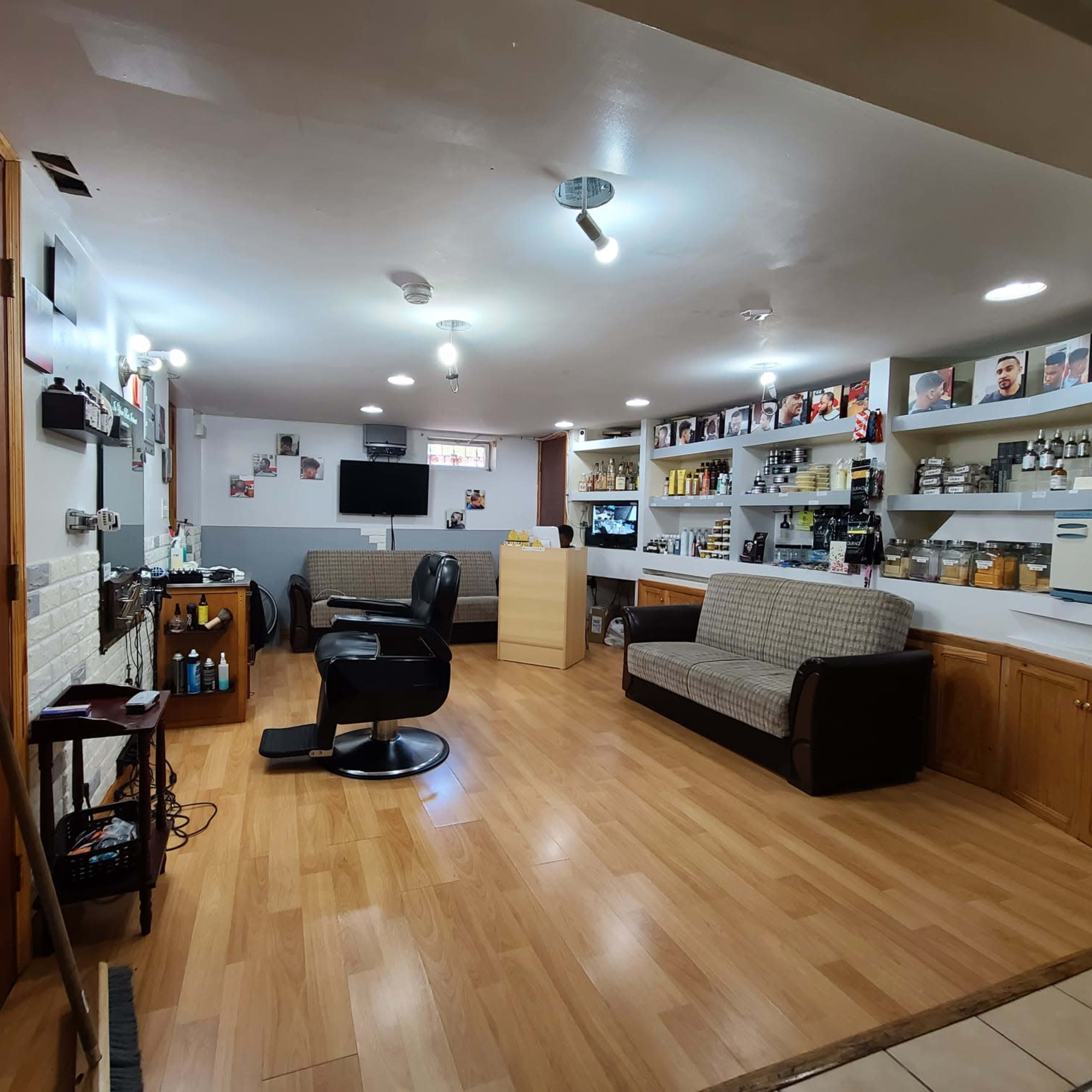 A basement room with two couches, a barber chair, shelves filled with bottles, and framed photos on the walls.