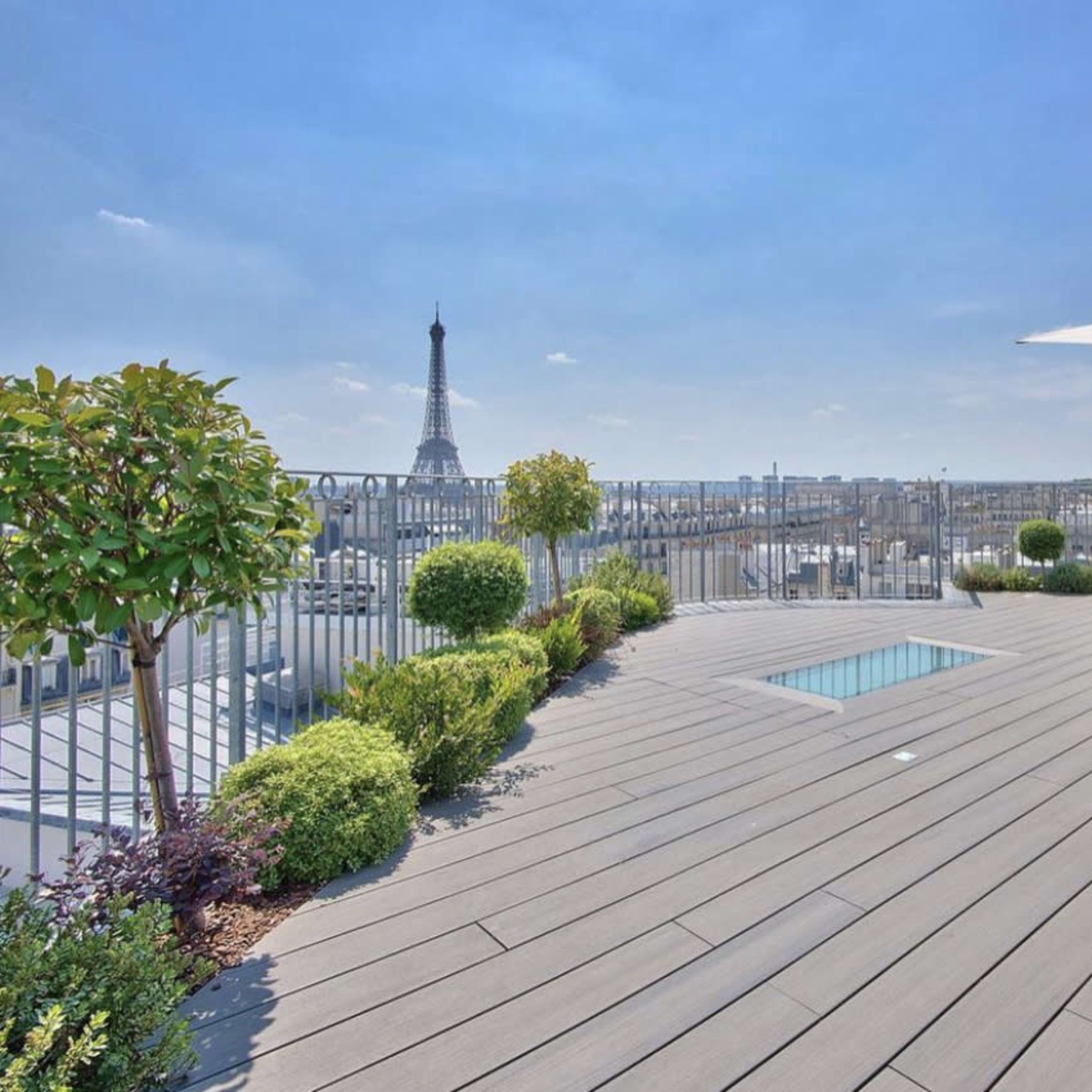 A rooftop terrace with a small swimming pool, lounge furniture, and a view of the Eiffel Tower in the background.
