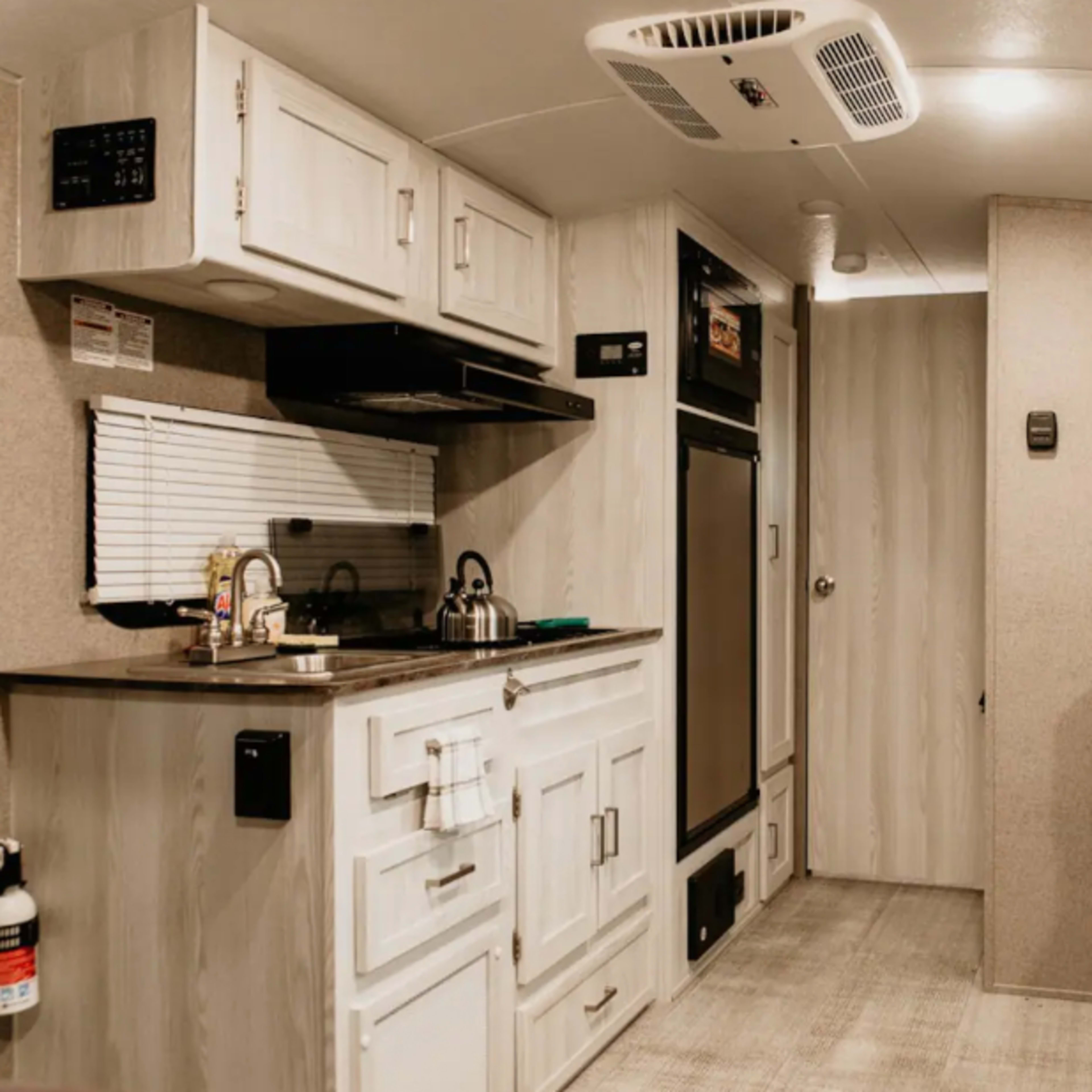 The interior of a modern camper trailer, featuring a kitchenette with a sink, stove, and refrigerator, along with a seating area and storage cabinets.