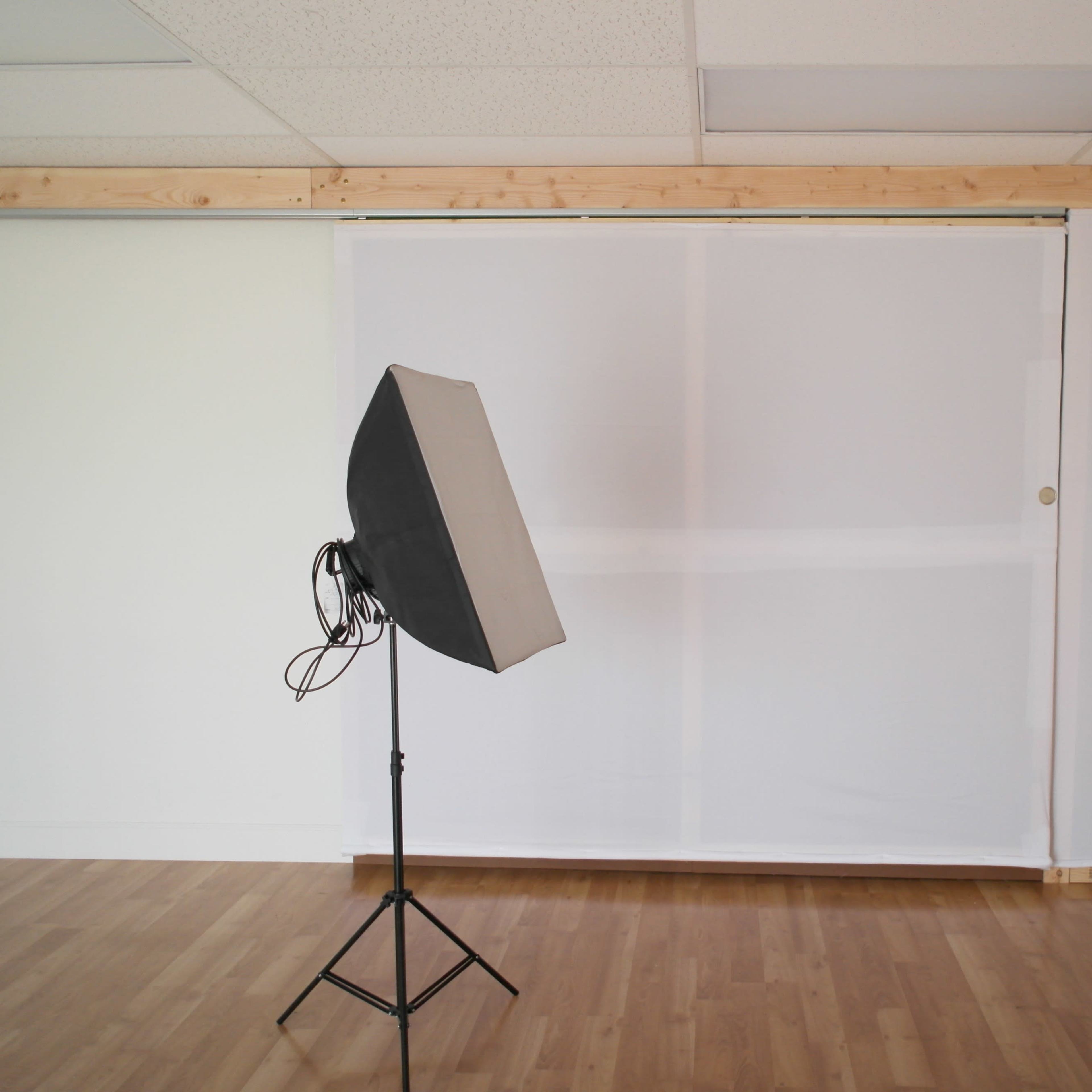 A photography studio features a softbox light positioned in front of a white backdrop and wooden paneling.