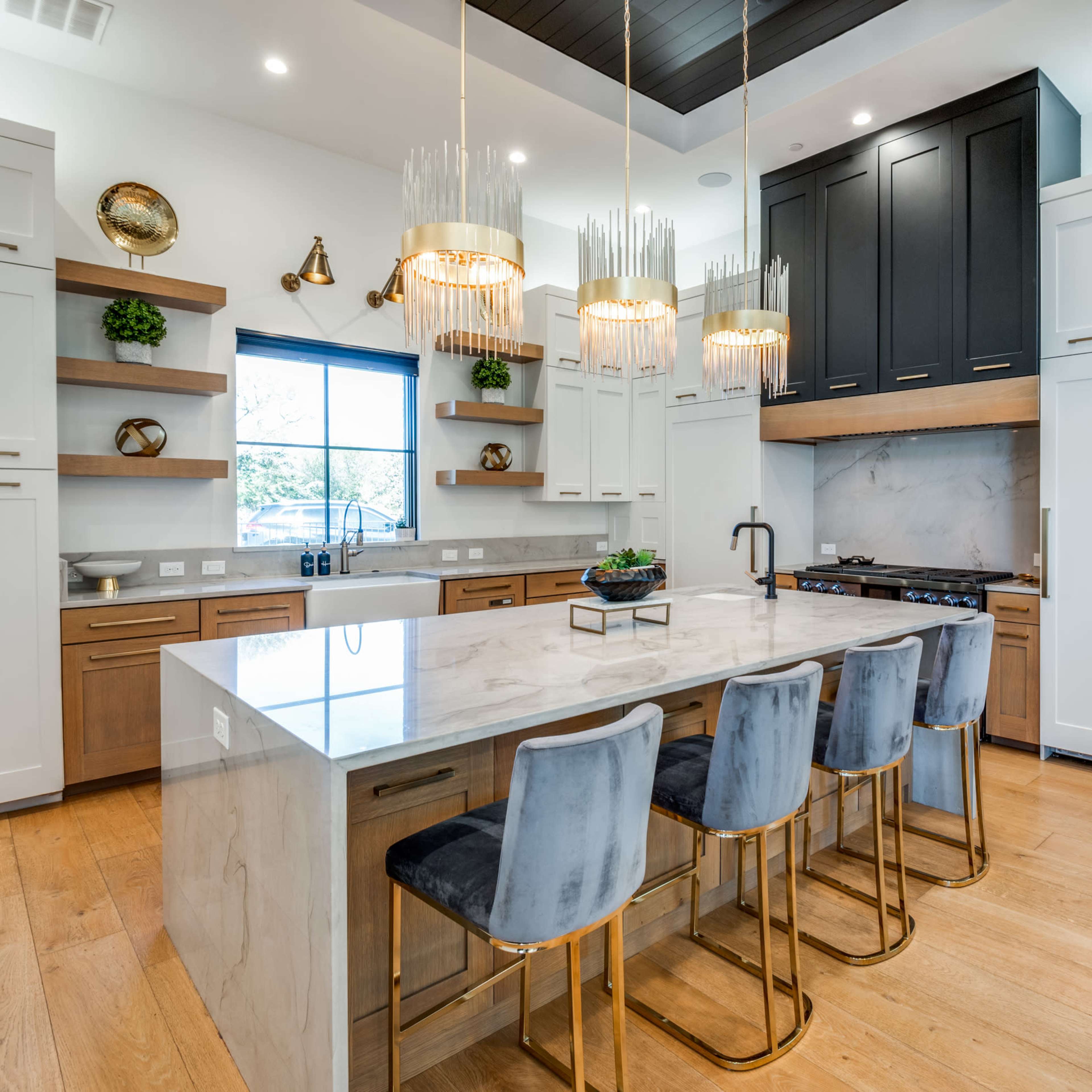 A modern kitchen featuring a large marble island with seating, sleek cabinetry in various colors, and pendant lighting above.