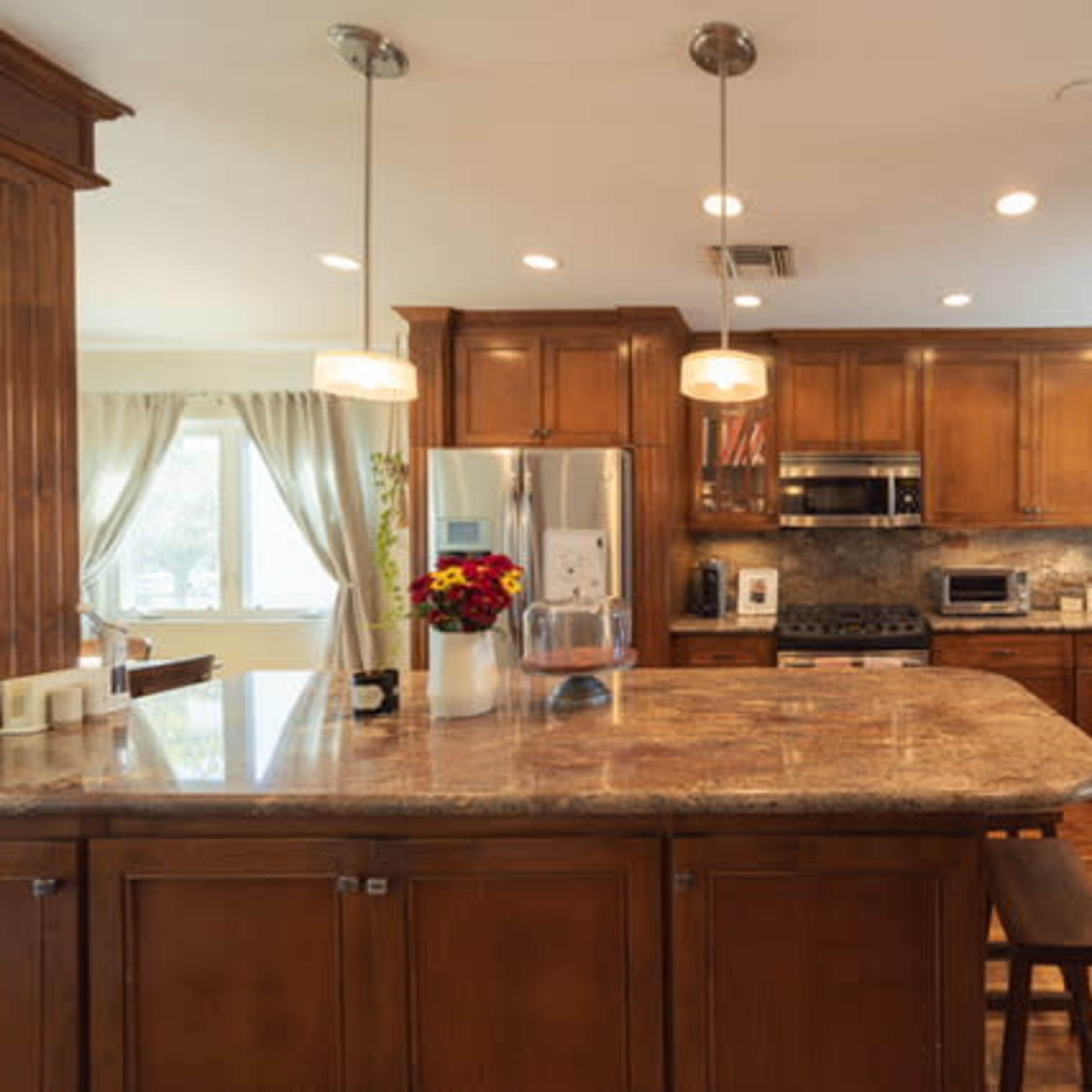 A modern kitchen features wooden cabinets, a large island with a granite countertop, and stainless steel appliances.