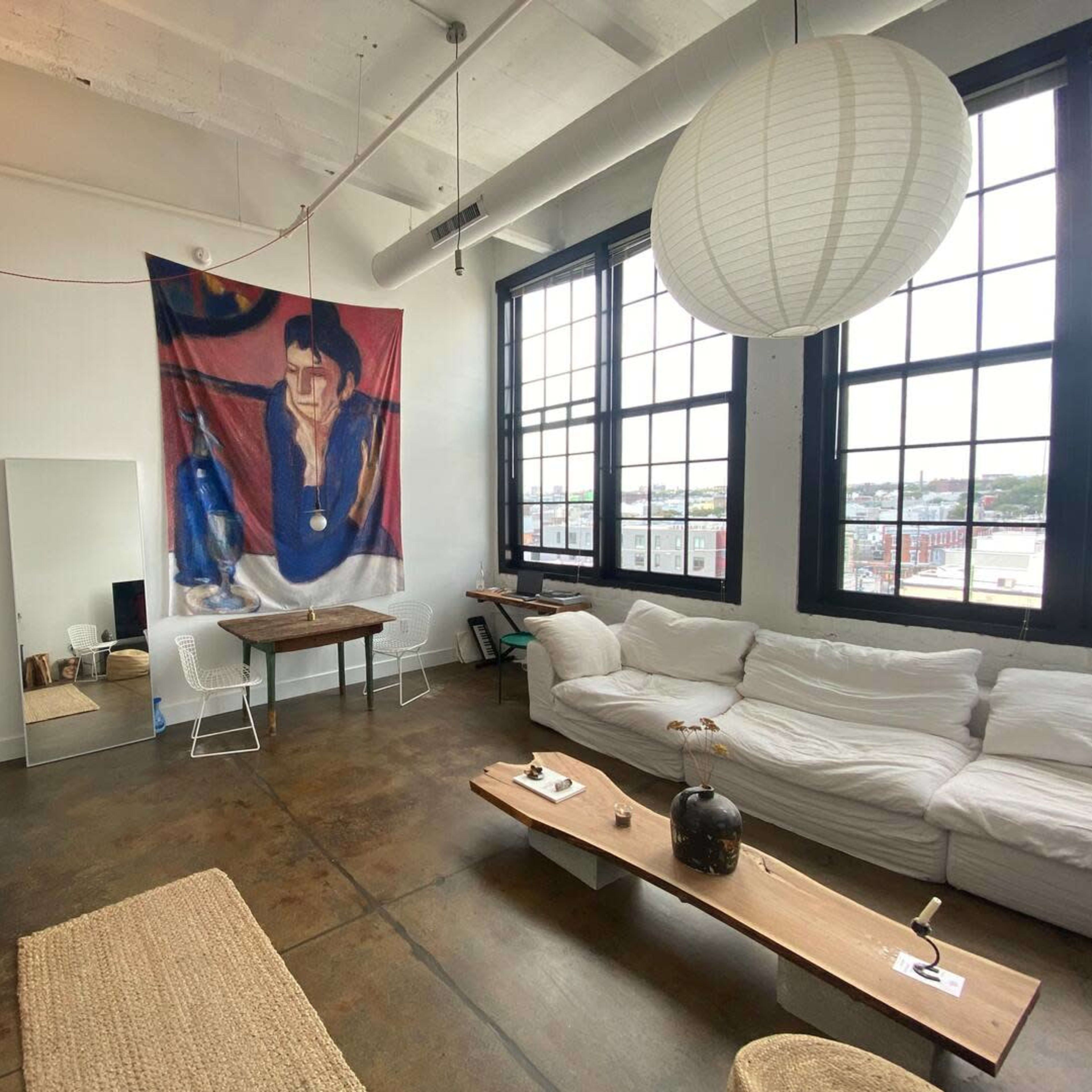 A modern loft features a spacious living area with a large banner hanging on the wall, a wooden table, a white couch, and large windows letting in natural light.