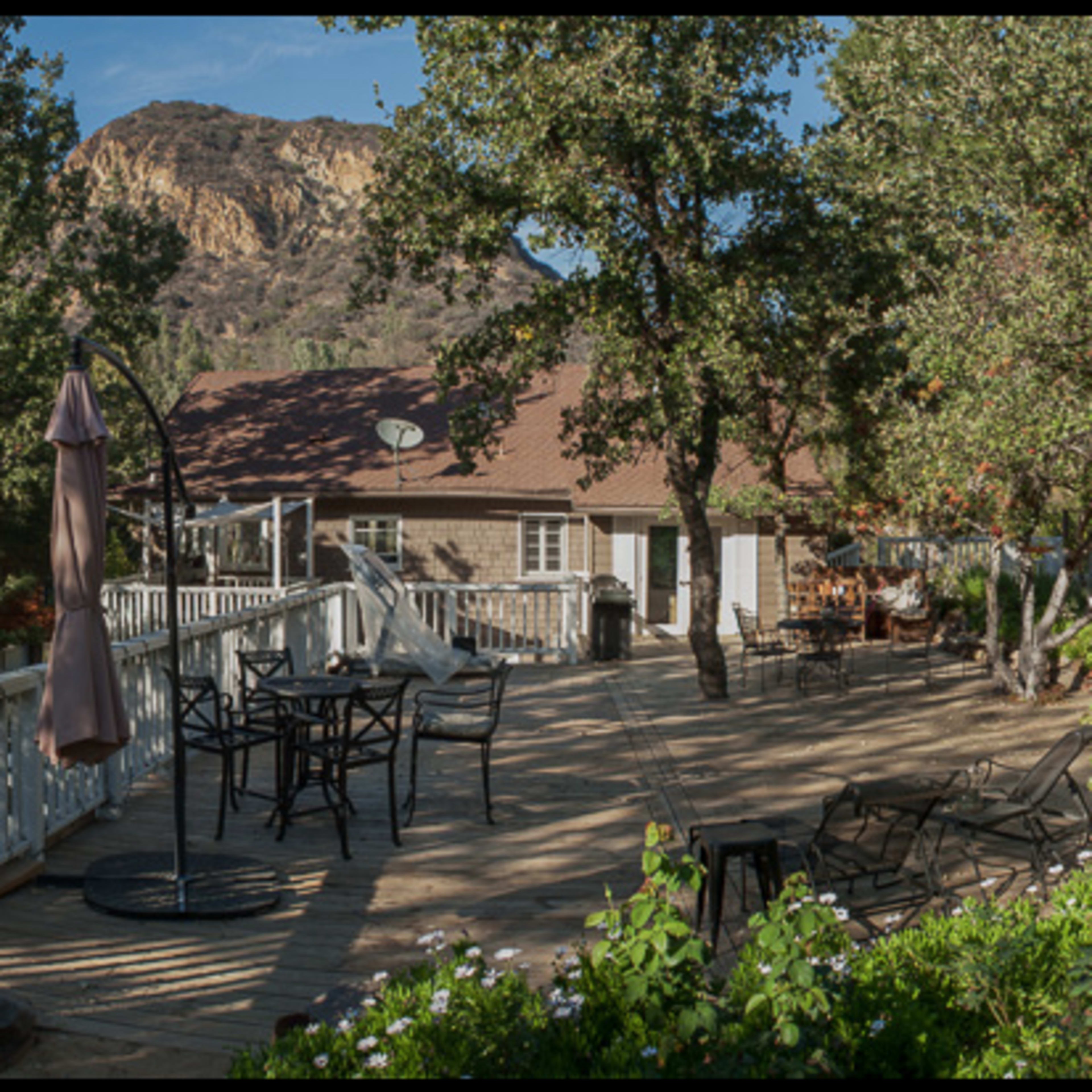 A wooden deck with outdoor seating and a garden area is surrounded by trees and overlooks a rocky hillside.