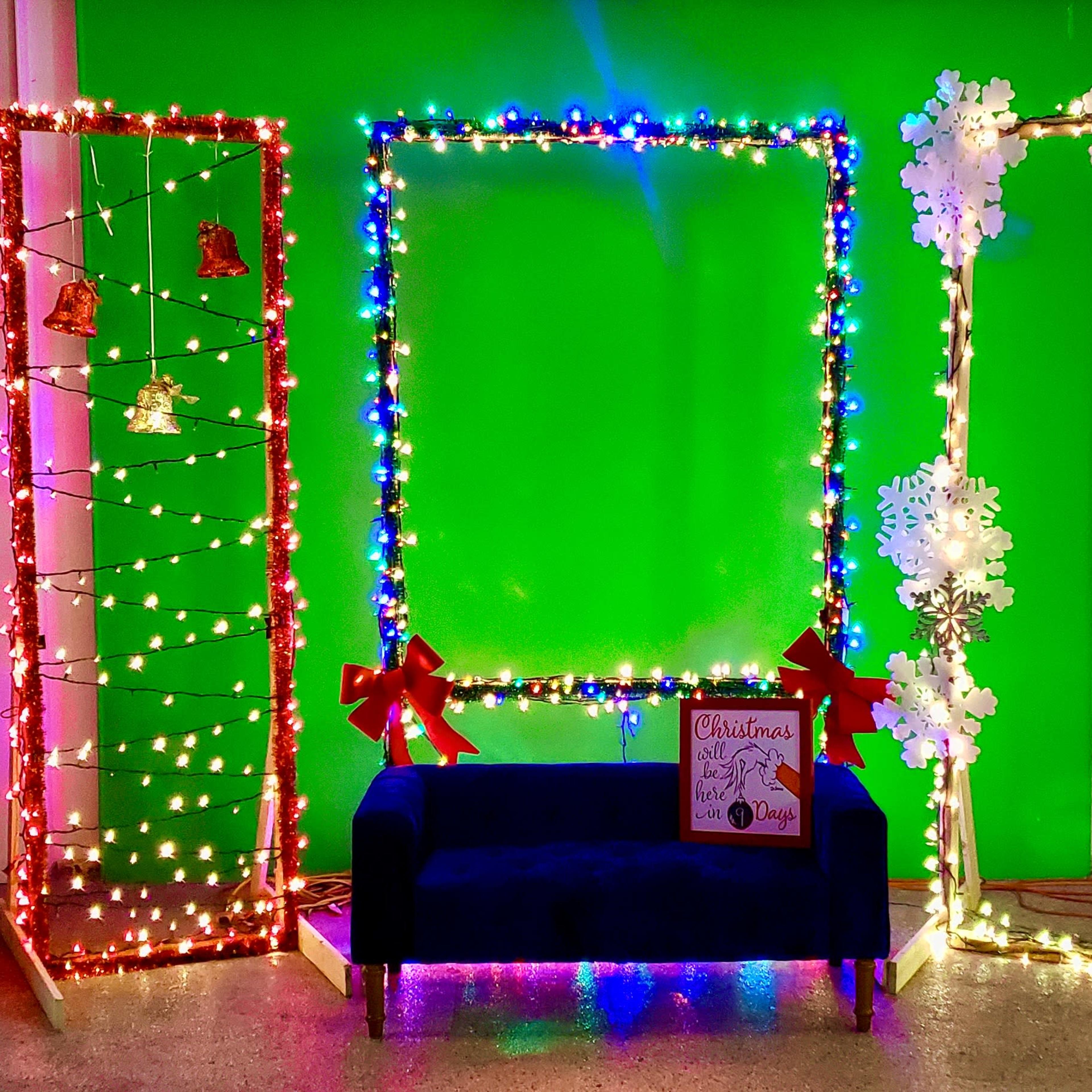 A vibrant holiday display with four lighted frames, a blue sofa in the center, and festive decorations including bells and snowflakes.