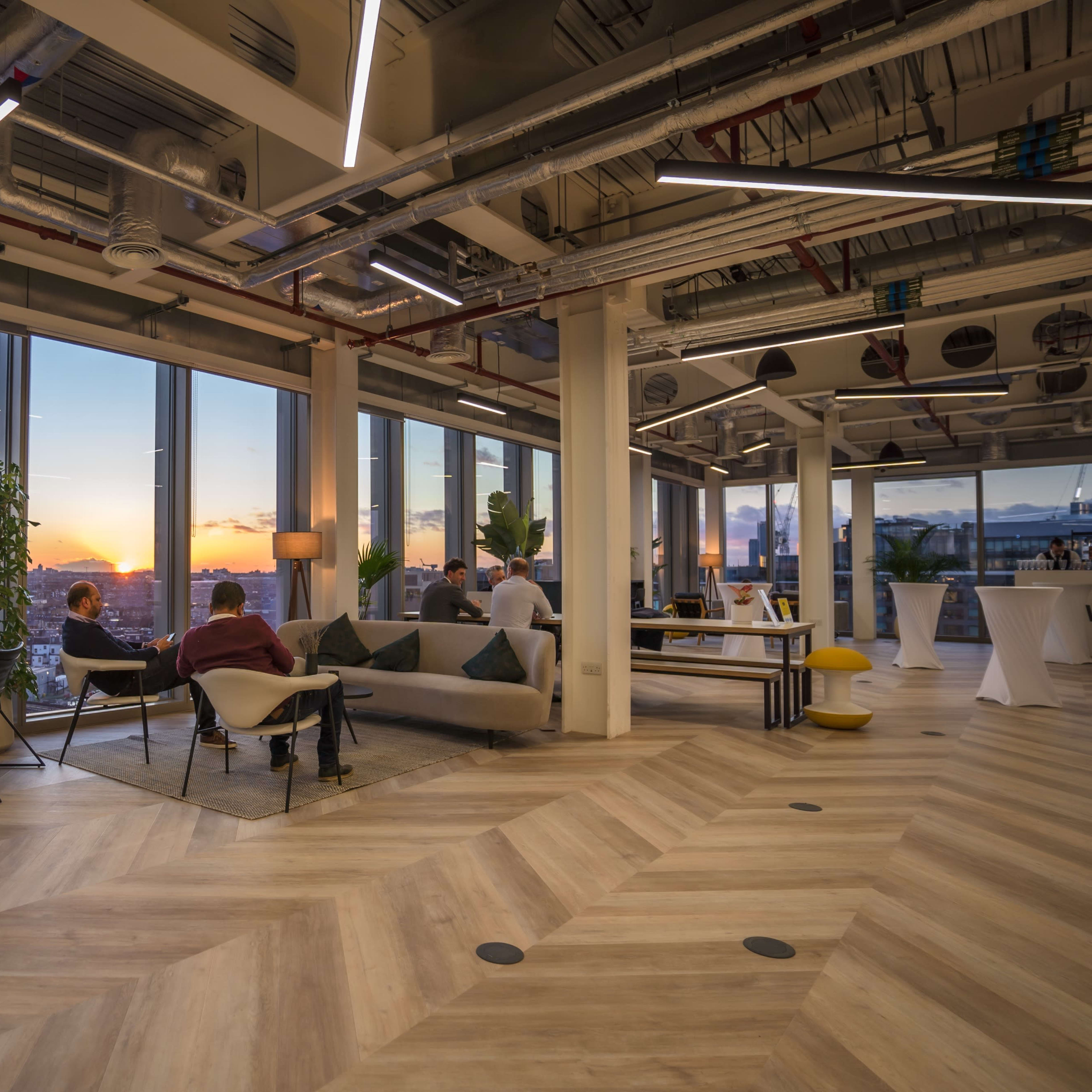 A modern office space featuring a seating area with large windows overlooking a cityscape at sunset.