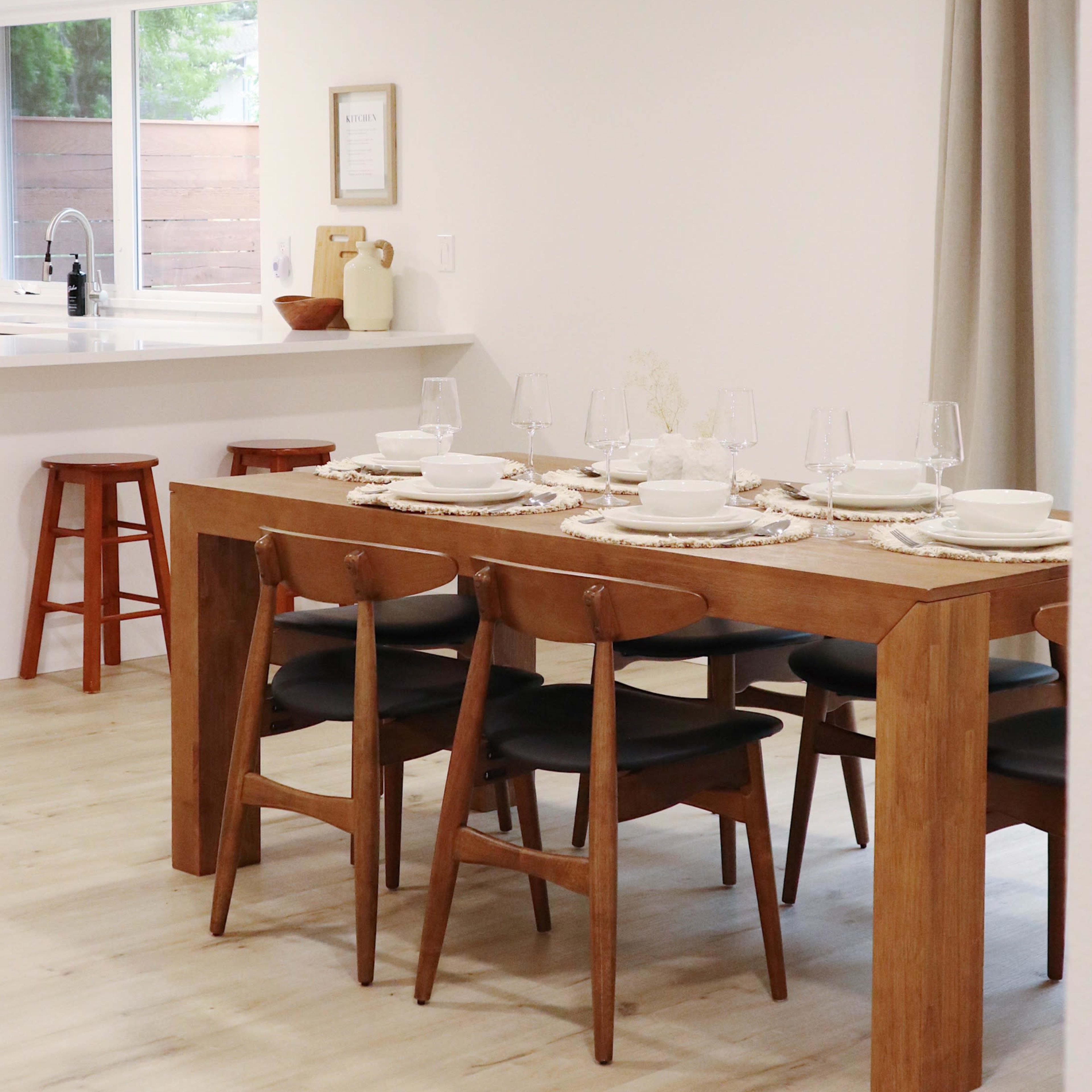 A modern dining area features a wooden table set for a meal with chairs and a window displaying a view of the outdoors.