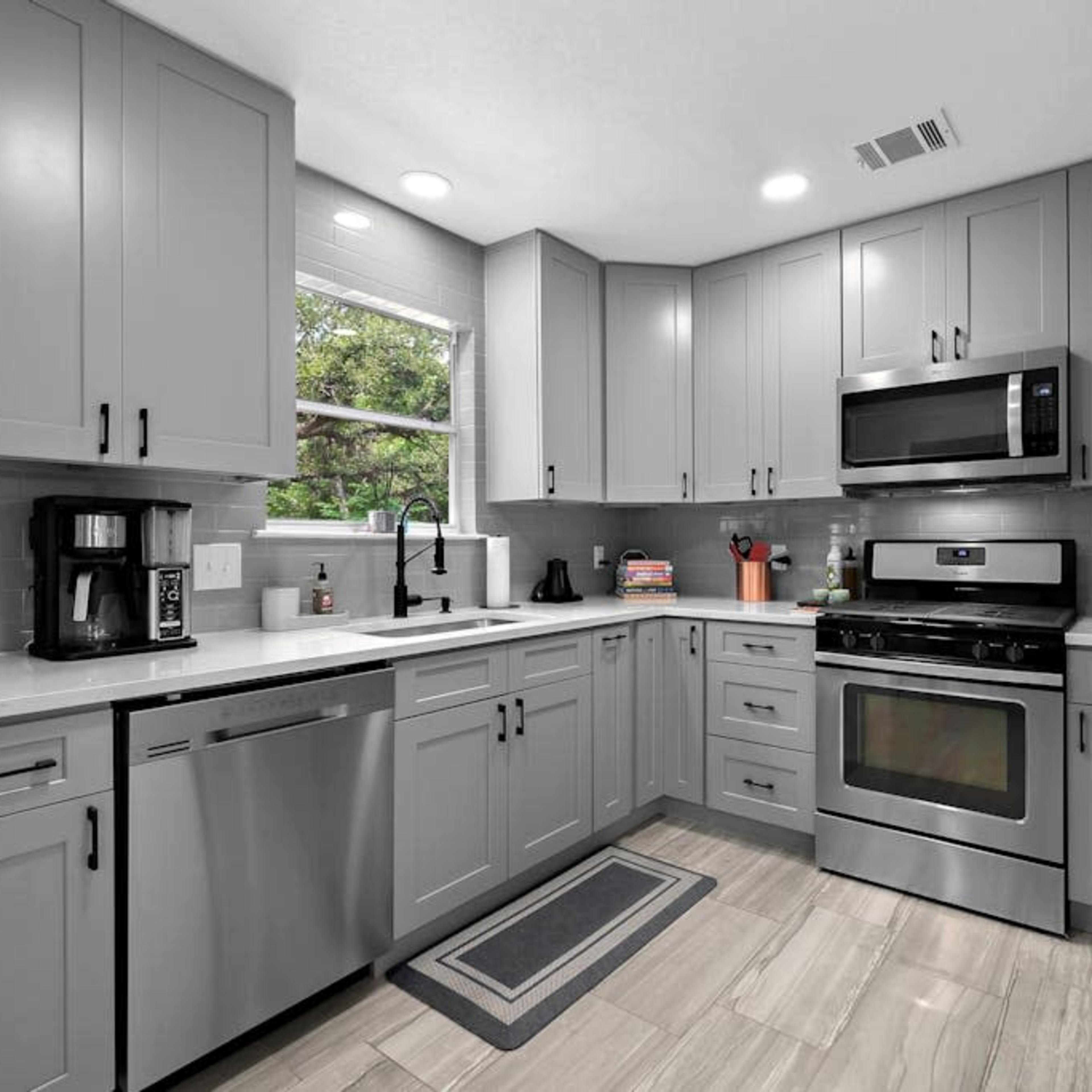 A modern kitchen with grey cabinets, stainless steel appliances, and a window providing natural light.