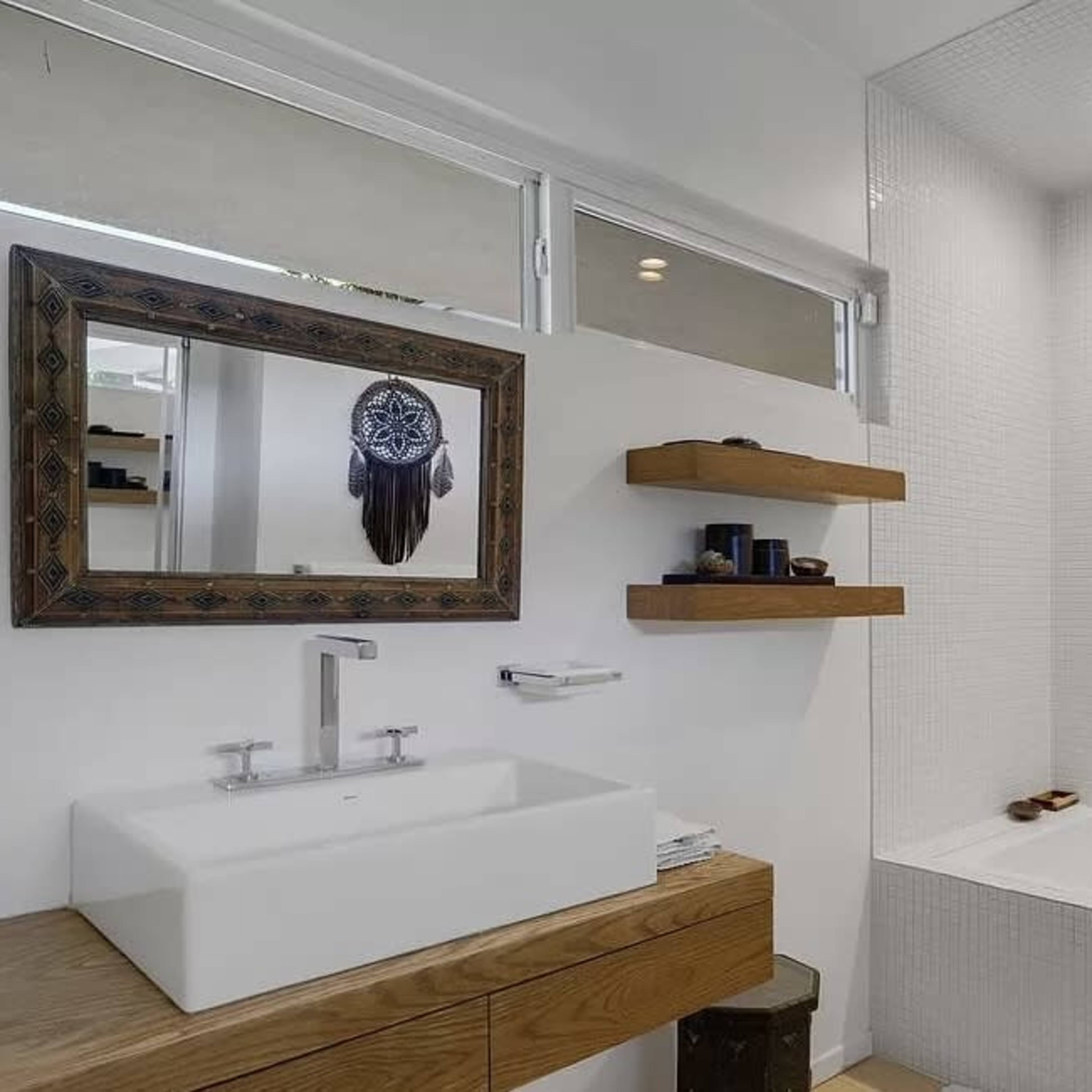 A modern bathroom featuring a white tiled shower area, a rectangular sink with an angular faucet, and wooden shelves displaying decorative items.