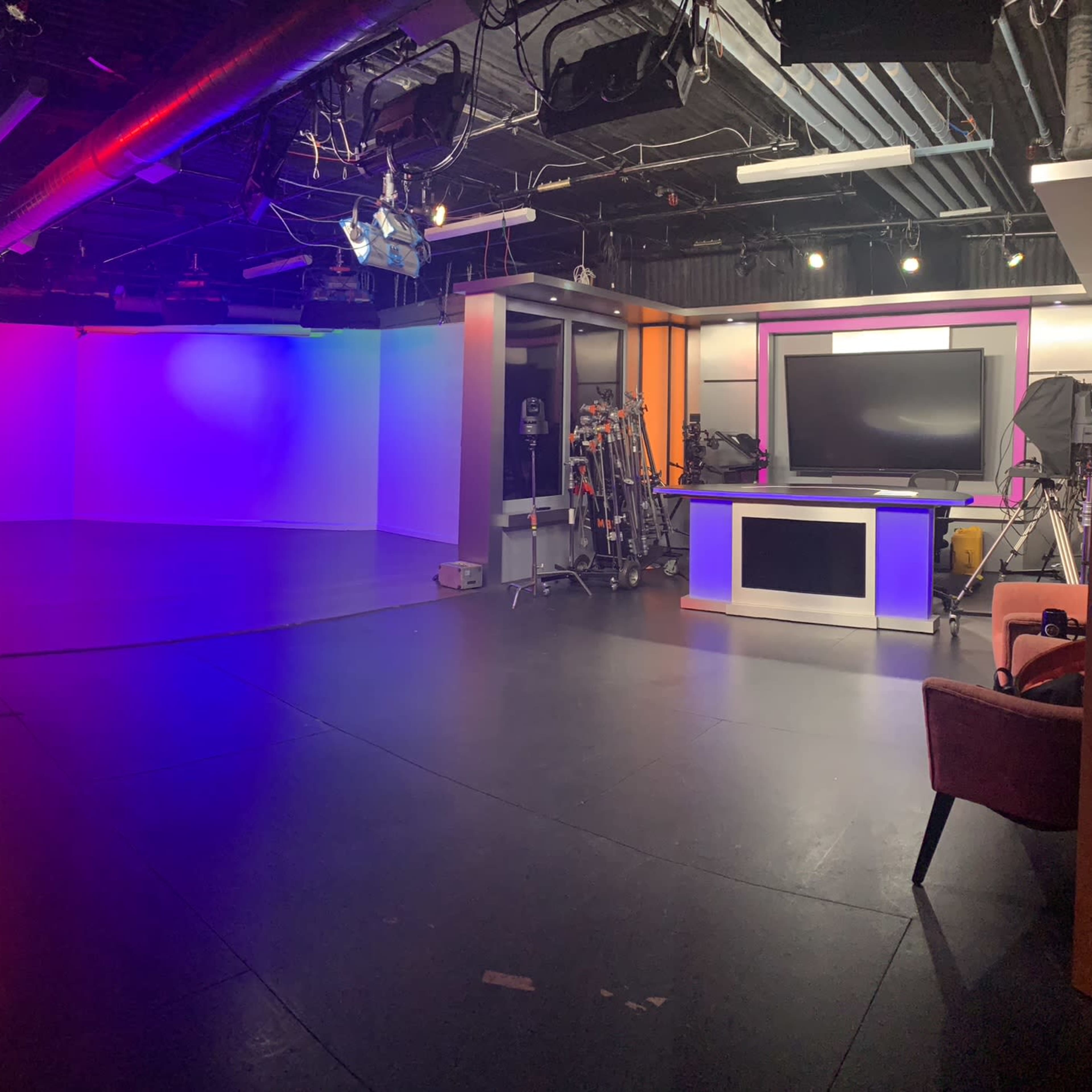 A well-lit television studio with colorful backdrops, various camera equipment, and a central news desk.
