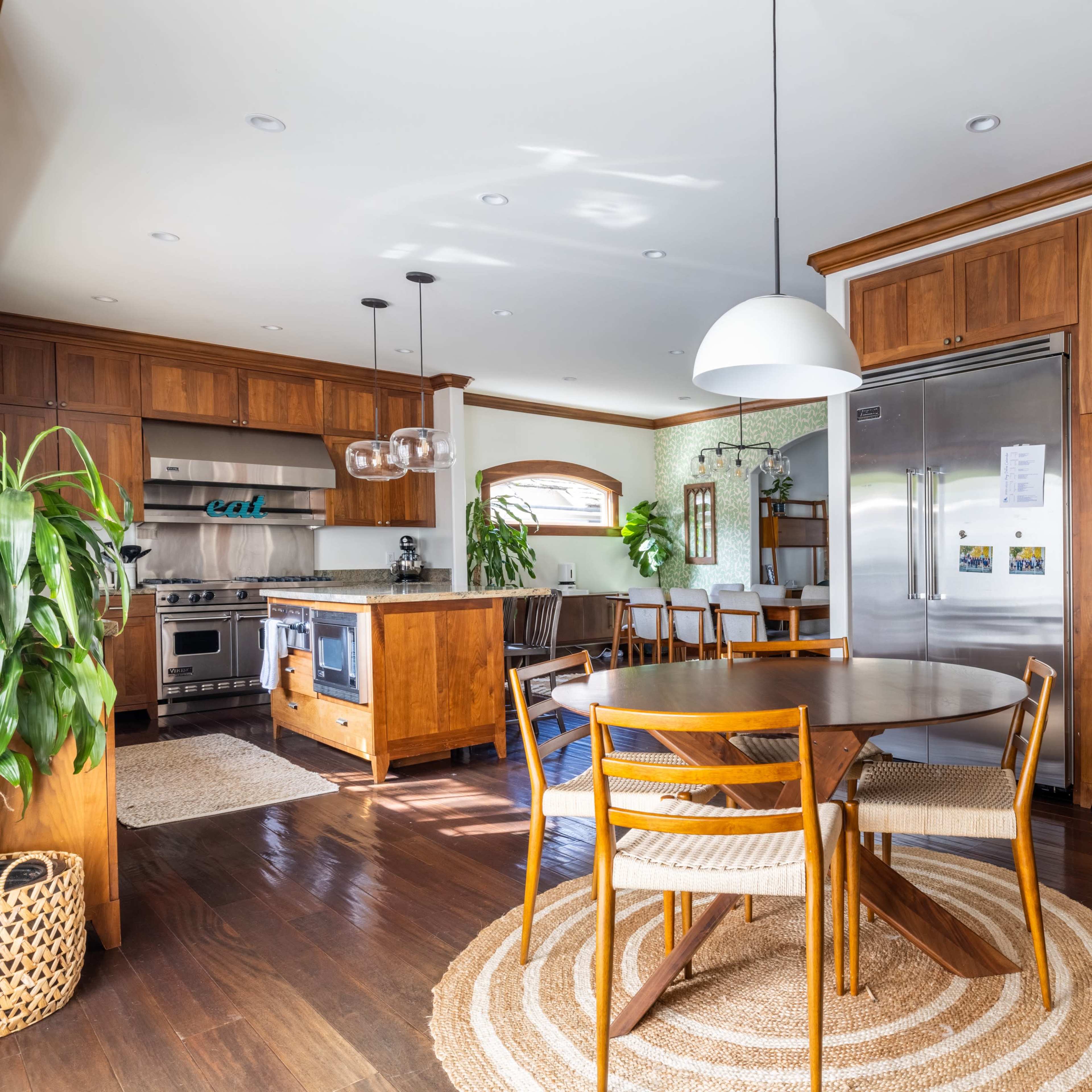 A modern kitchen and dining area features wooden cabinetry, a circular table with four chairs, and a staircase in the corner.
