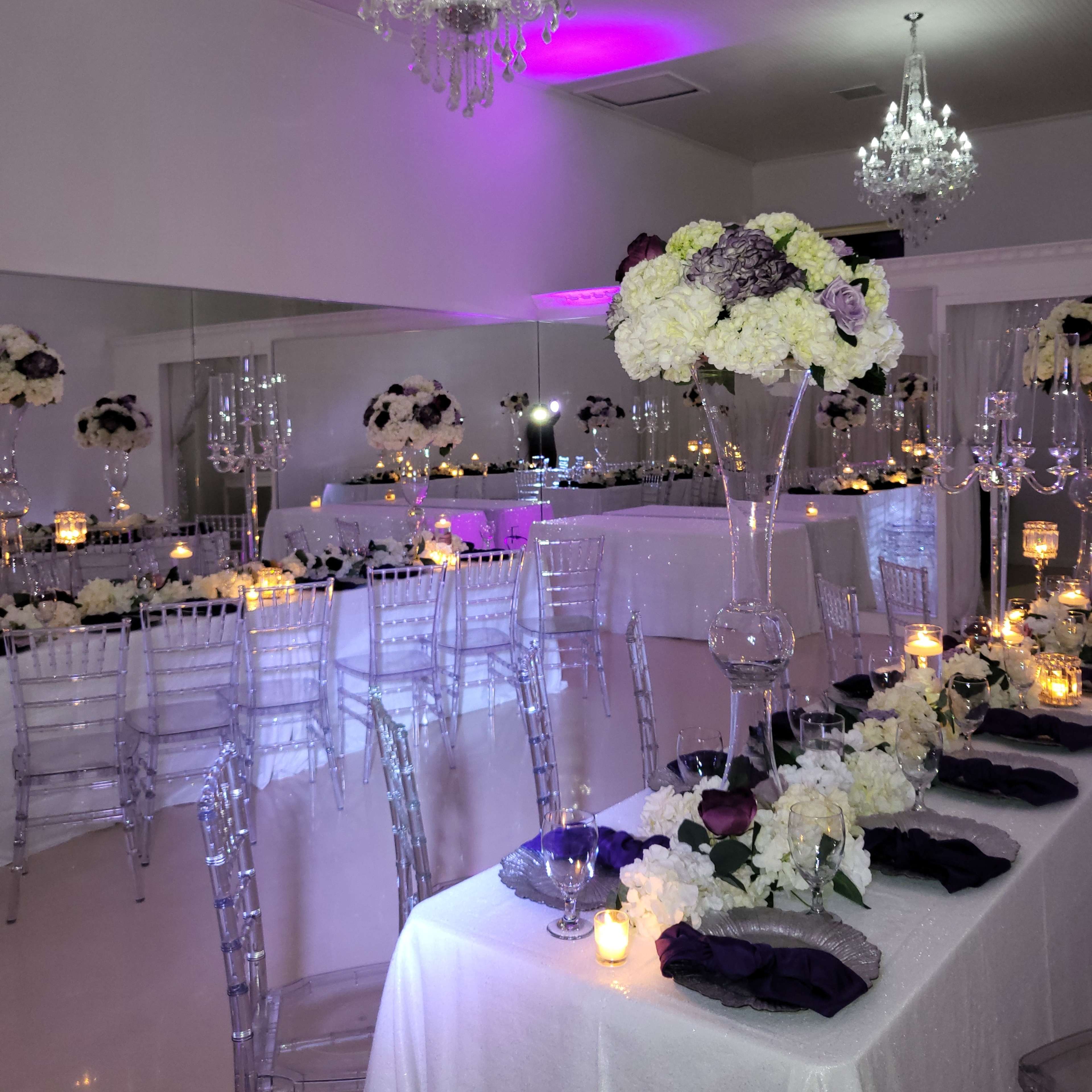 An elegantly decorated event space with mirrored walls, crystal chandeliers, and tables adorned with floral centerpieces and soft lighting.