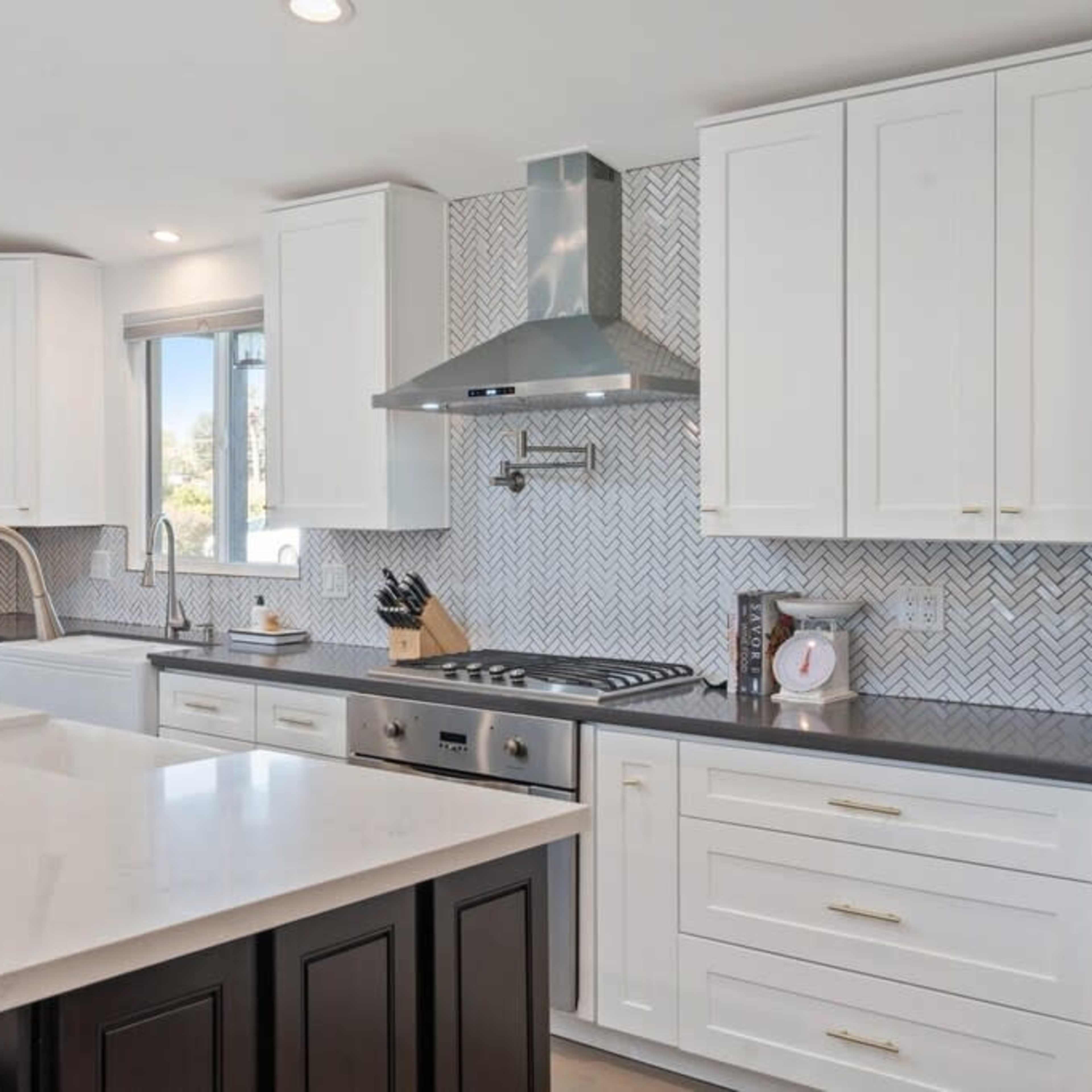 The kitchen features a central island with a white countertop, stainless steel appliances, and white cabinetry against a patterned backsplash.