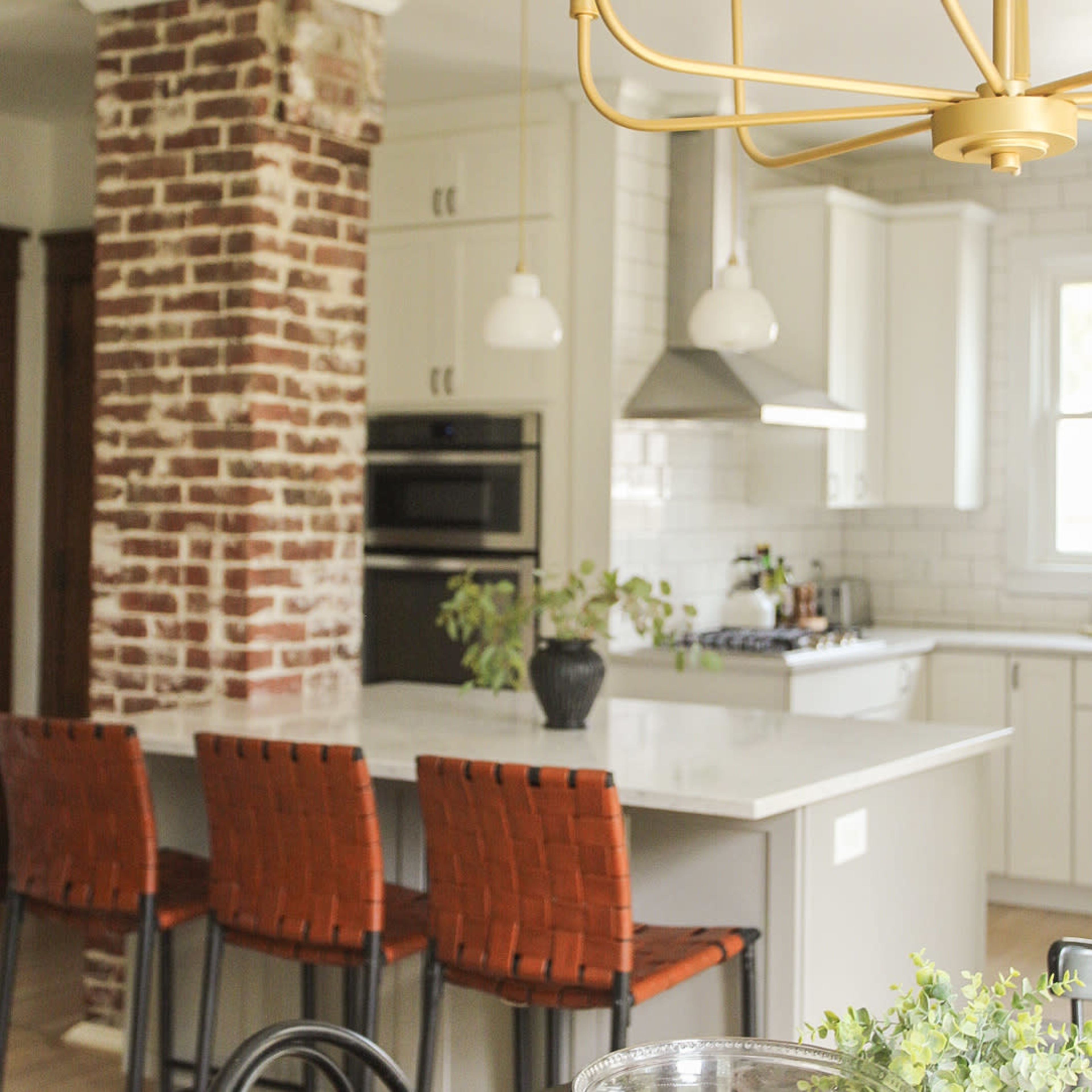 A modern kitchen with a brick accent wall, white cabinetry, and four brown woven bar stools at a kitchen island.